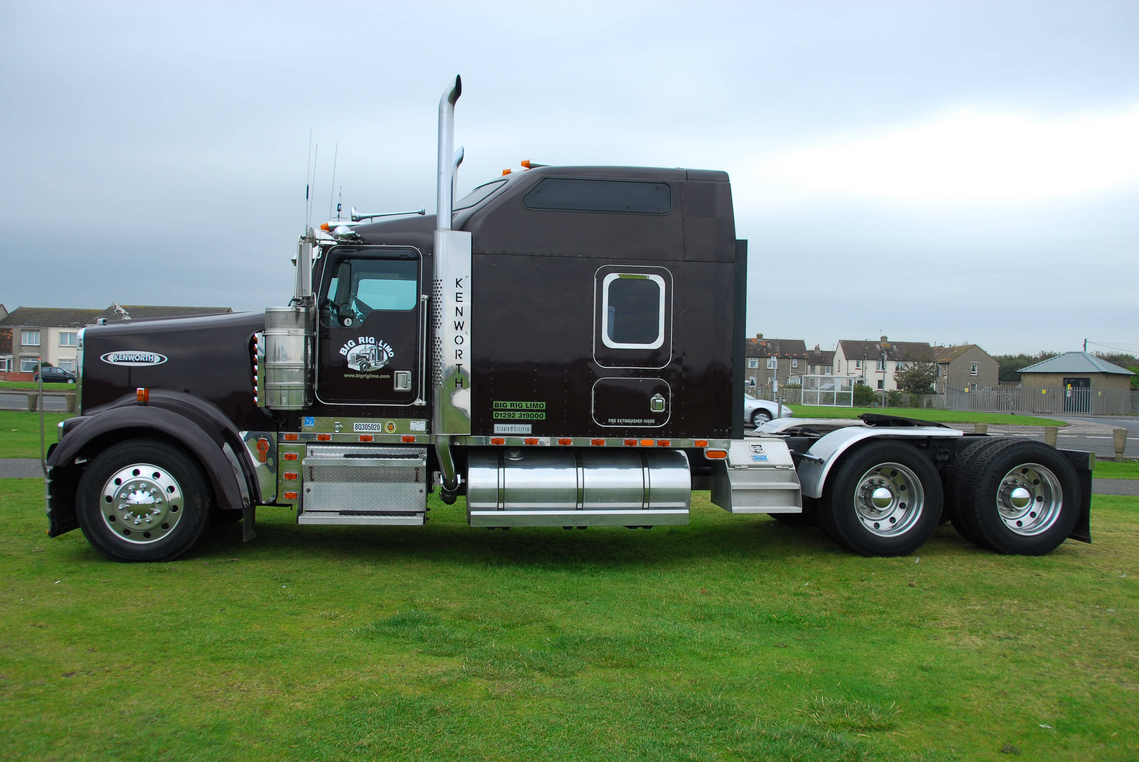 Kenworth W900 桌布 壁紙 — 一輛時尚的黑色Kenworth半掛卡車帶有鍍鉻裝飾，停泊在陰天下的草地上。