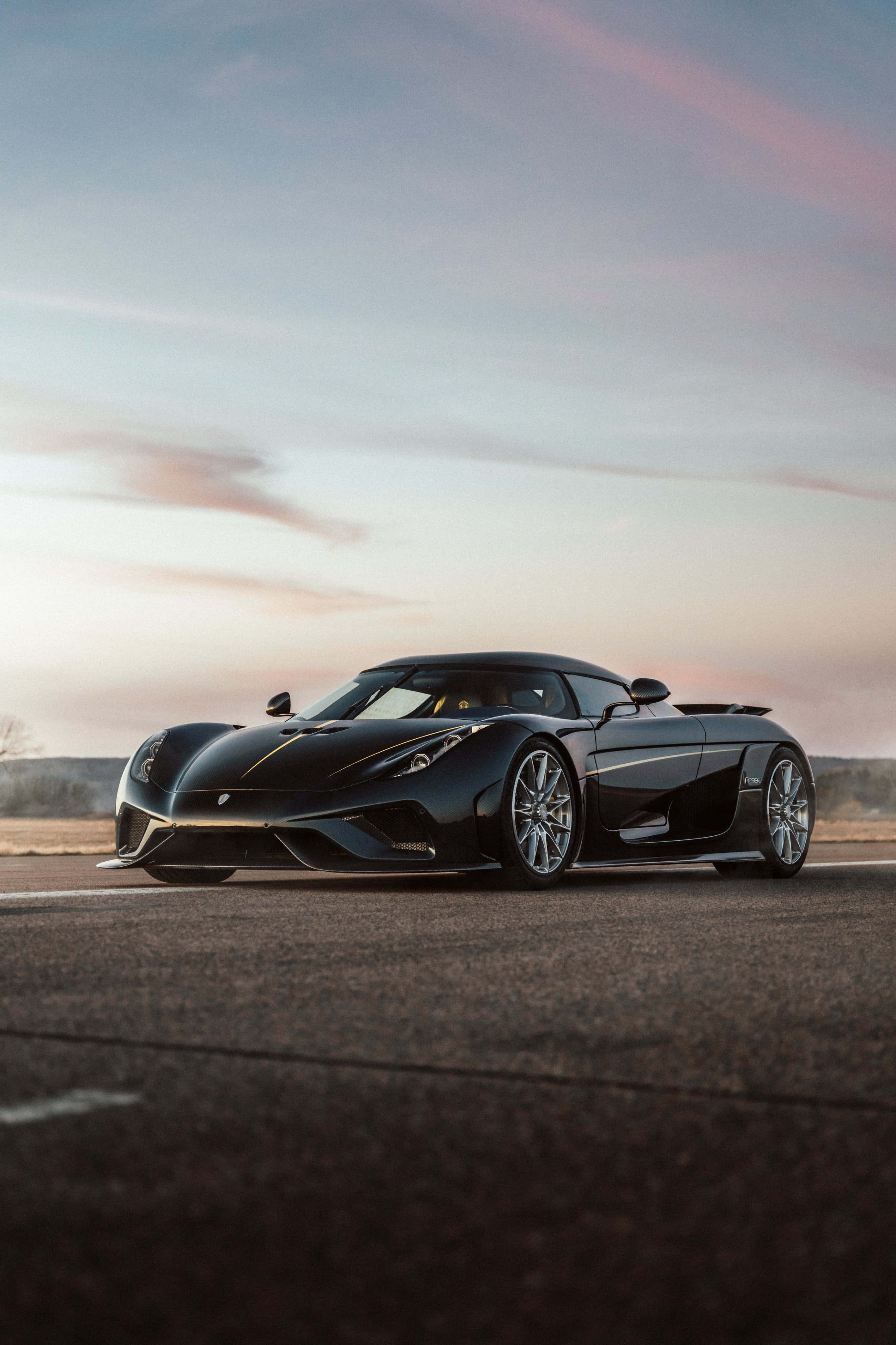 Koenigsegg 桌布 壁紙 — 一輛時尚的黑色Koenigsegg超級跑車在柔和的粉紅色和藍色暮色天空下，在開闊的道路上閃閃發光。