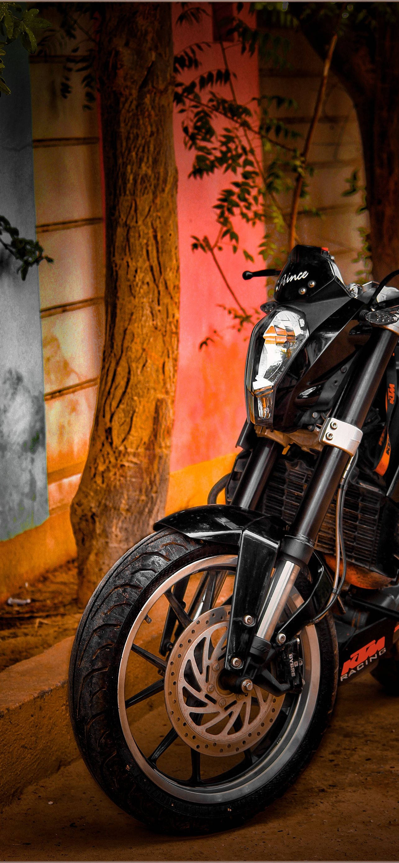 ktm rc 200 桌布 壁紙 — 一輛時尚的黑色KTM摩托車停在一棵樹旁，在溫暖的環境燈光下，以色彩繽紛的牆壁為背景。