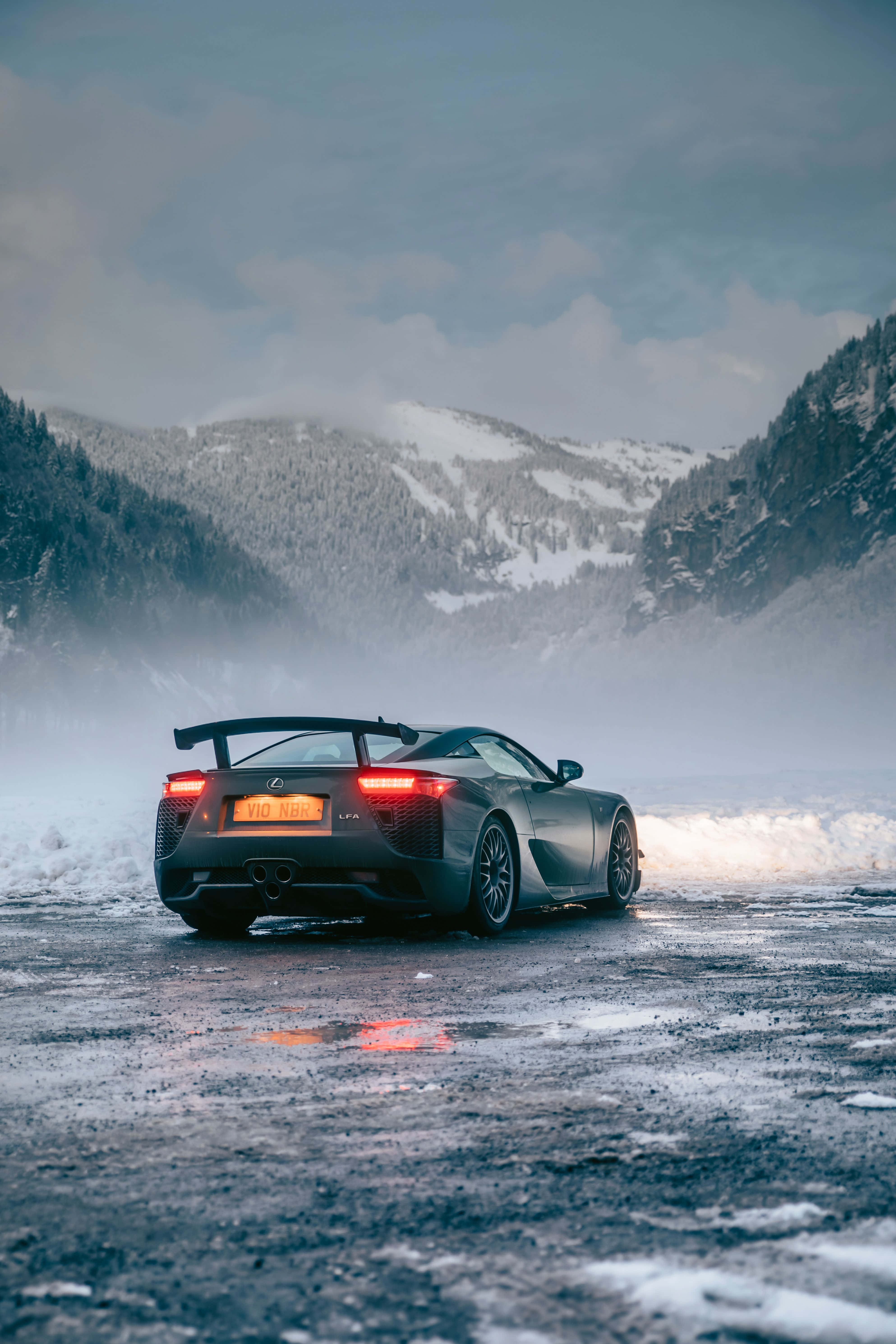 Lexus Lfa 桌布 壁紙 — 一輛時尚的黑色Lexus LFA在白雪覆蓋的山路上飄移，紅色尾燈在霧氣繚繞的山峰間閃耀。