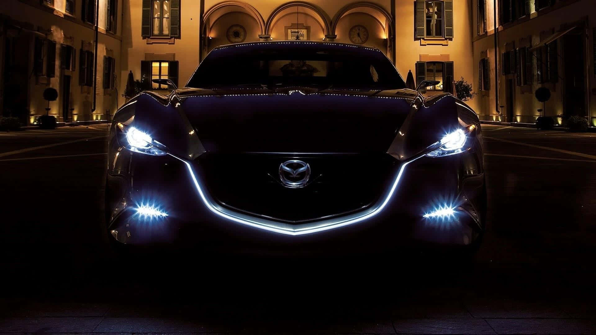 Mazda Rx-8 桌布 壁紙 — 一輛時尚的黑色Mazda跑車在夜間停在優雅的拱形建築前，發出明亮的白色頭燈和底盤燈光。
