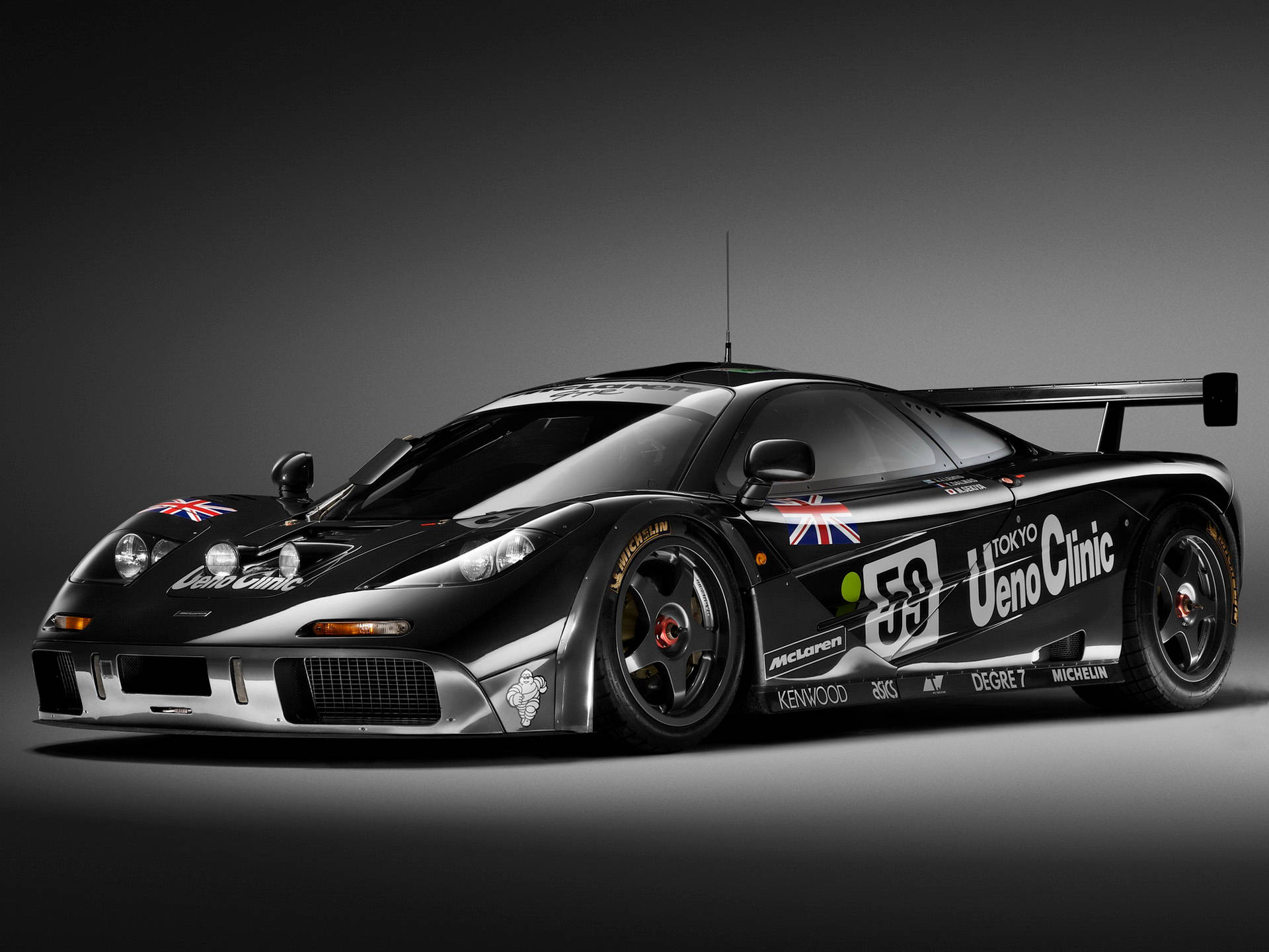酷炫F1 桌布 壁紙 — 一輛時尚的黑色McLaren F1 GTR賽車，帶有英國國旗和贊助商貼紙，在漸變灰色工作室背景前擺姿勢。