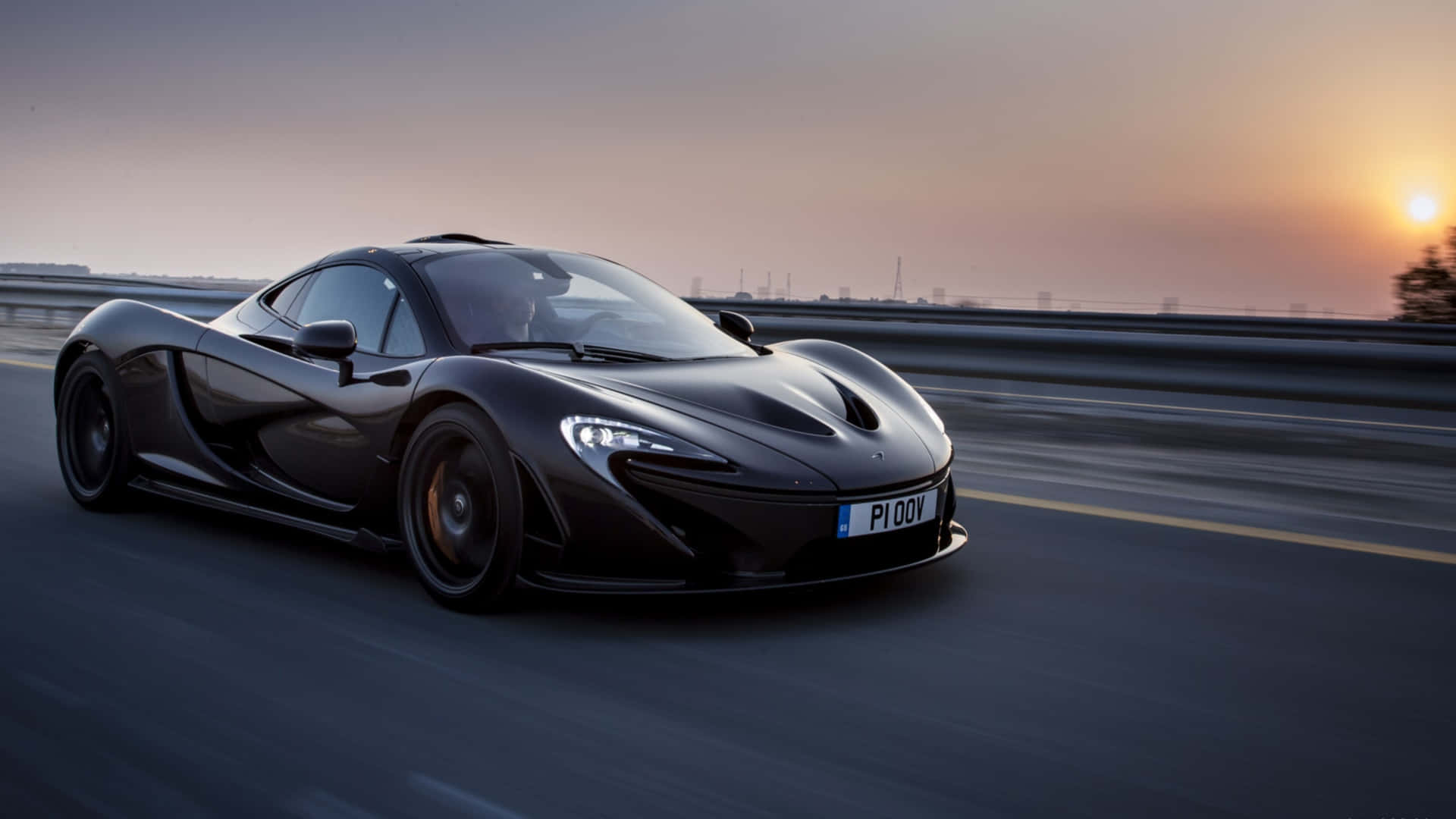 麥拉倫 桌布 壁紙 — 一輛時尚的黑色McLaren P1在日落時分沿著高速公路疾馳，帶有模糊的動態和溫暖的天空色調。