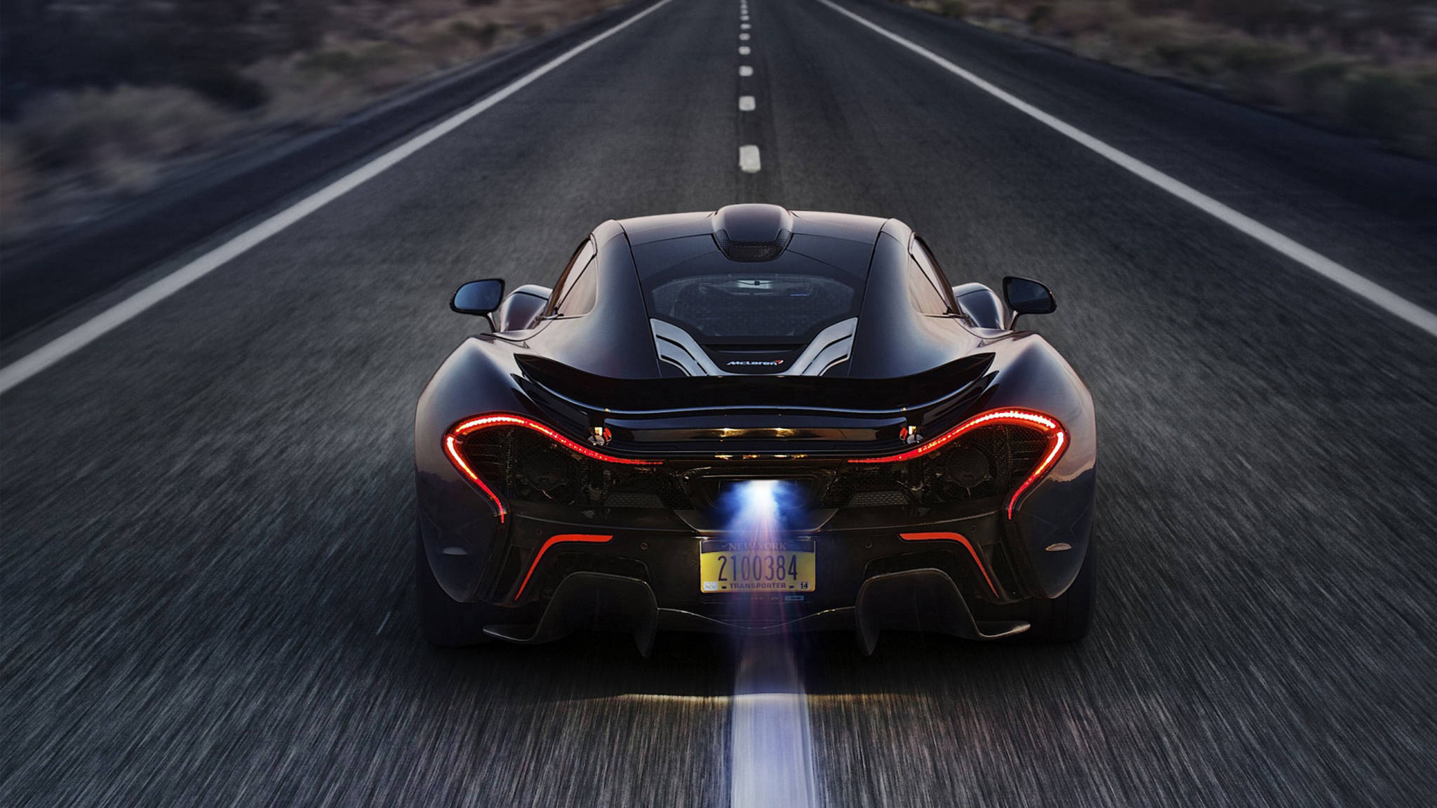 cars 桌布 壁紙 — 一輛時尚的黑色McLaren跑車在沙漠公路上飛馳，紅色尾燈閃爍，藍色排氣火焰噴射。