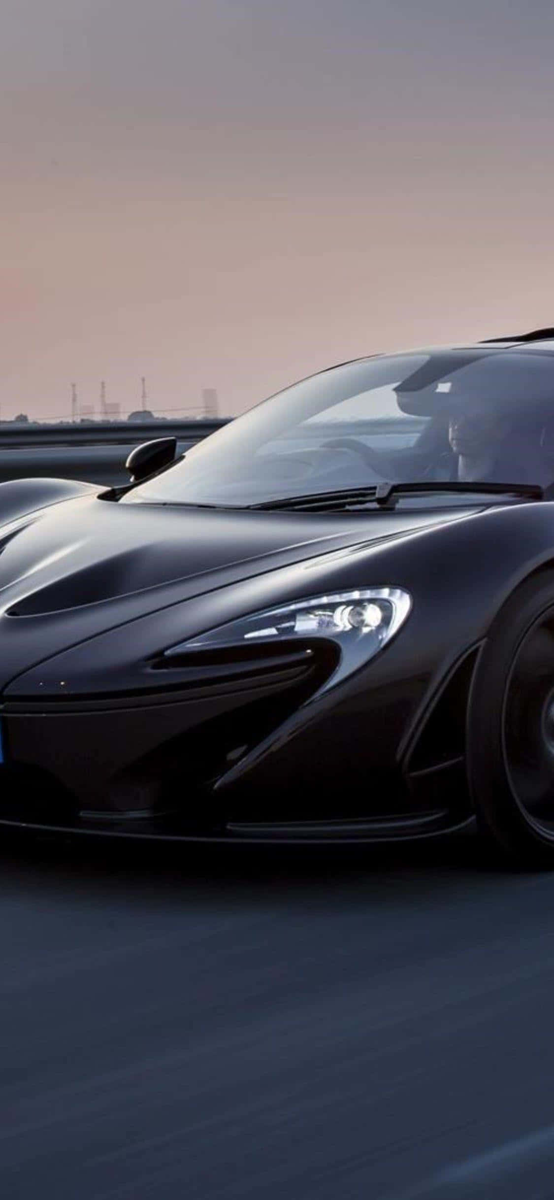 iPhone Xs Mclaren 720s 桌布 壁紙 — 一輛時尚的黑色McLaren跑車在柔和暮色下的高速公路上高速行駛。