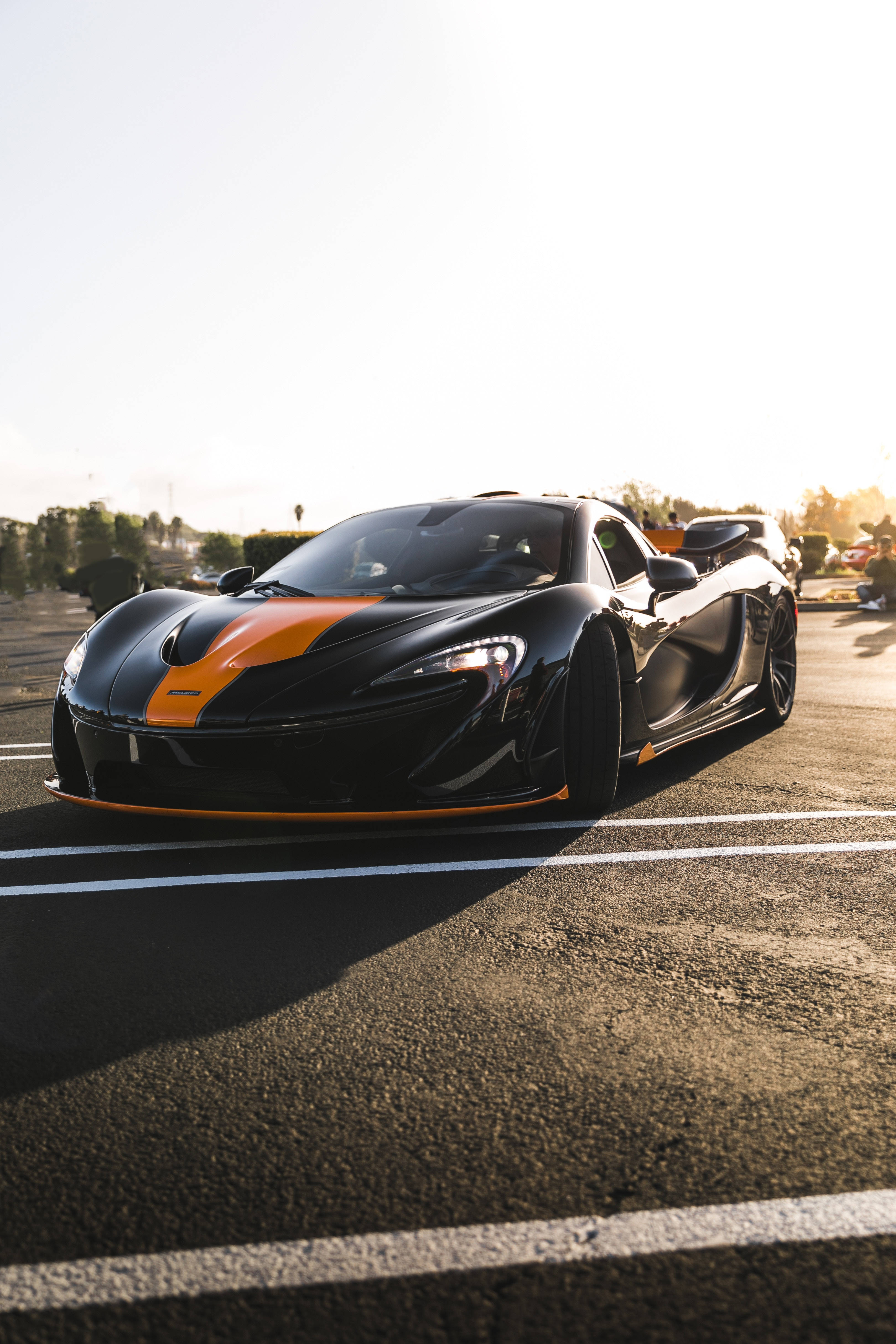 Luxury 桌布 壁紙 — 一輛時尚的黑色McLaren跑車，帶有橙色點綴，停在瀝青路上，沐浴在金色的夕陽光中。