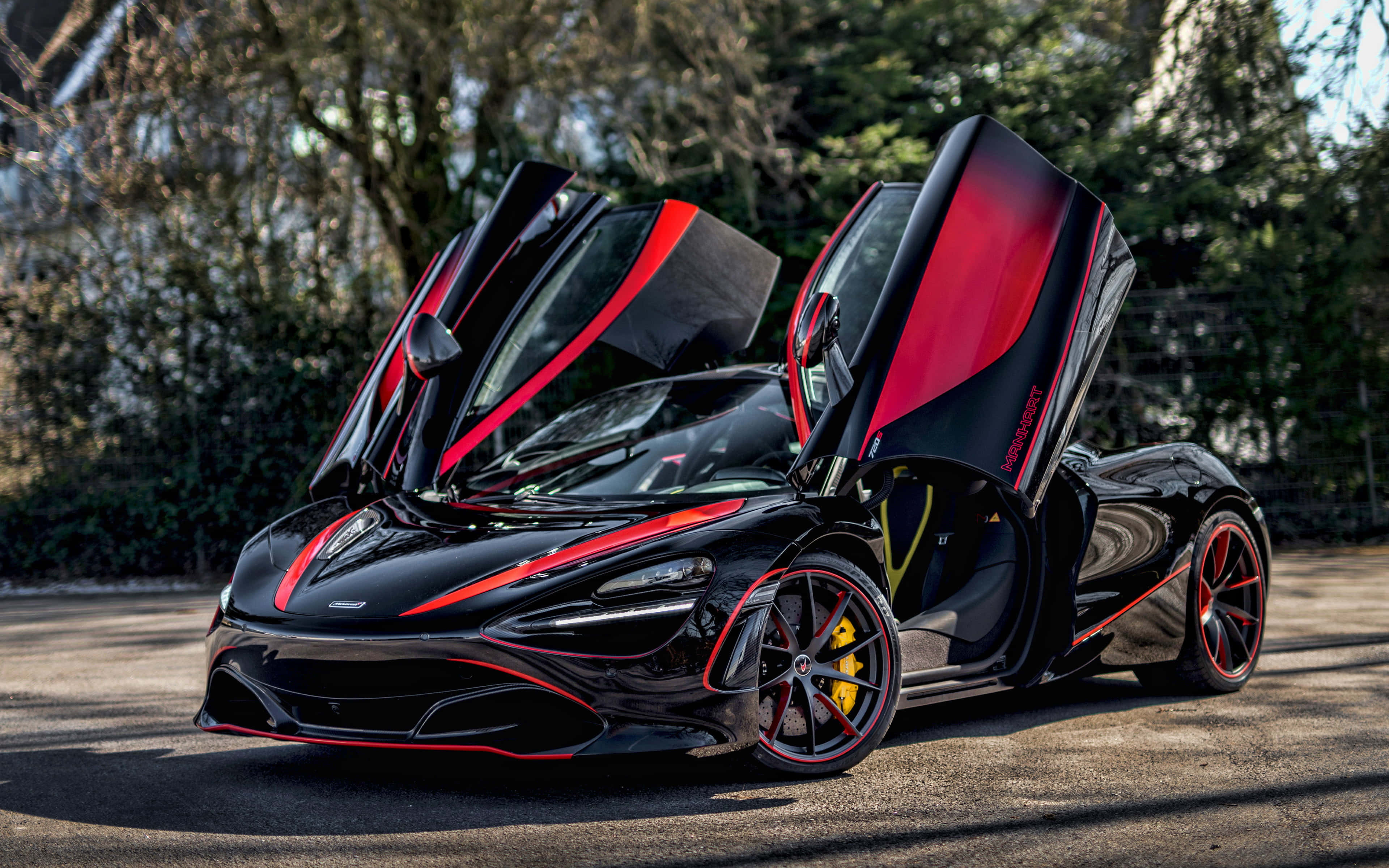 Mclaren 720s 桌布 壁紙 — 一輛時尚的黑色McLaren跑車，帶有紅色點綴和打開的蝴蝶門，停泊在陽光普照、樹木環繞的車道上。