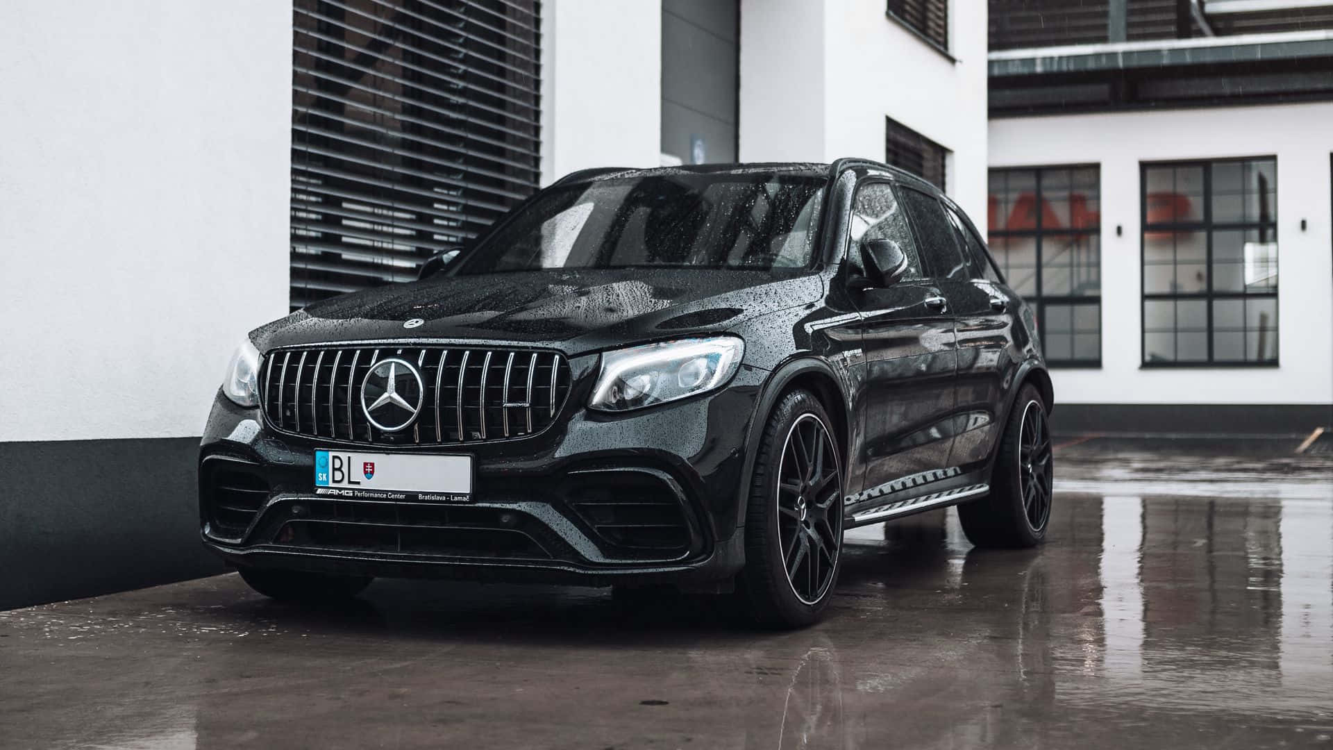 主題 桌布 壁紙 — 一輛時尚的黑色Mercedes-AMG GLC 63 S停在濕漉漉的路面上，在現代白色建築的映襯下反射出光澤。