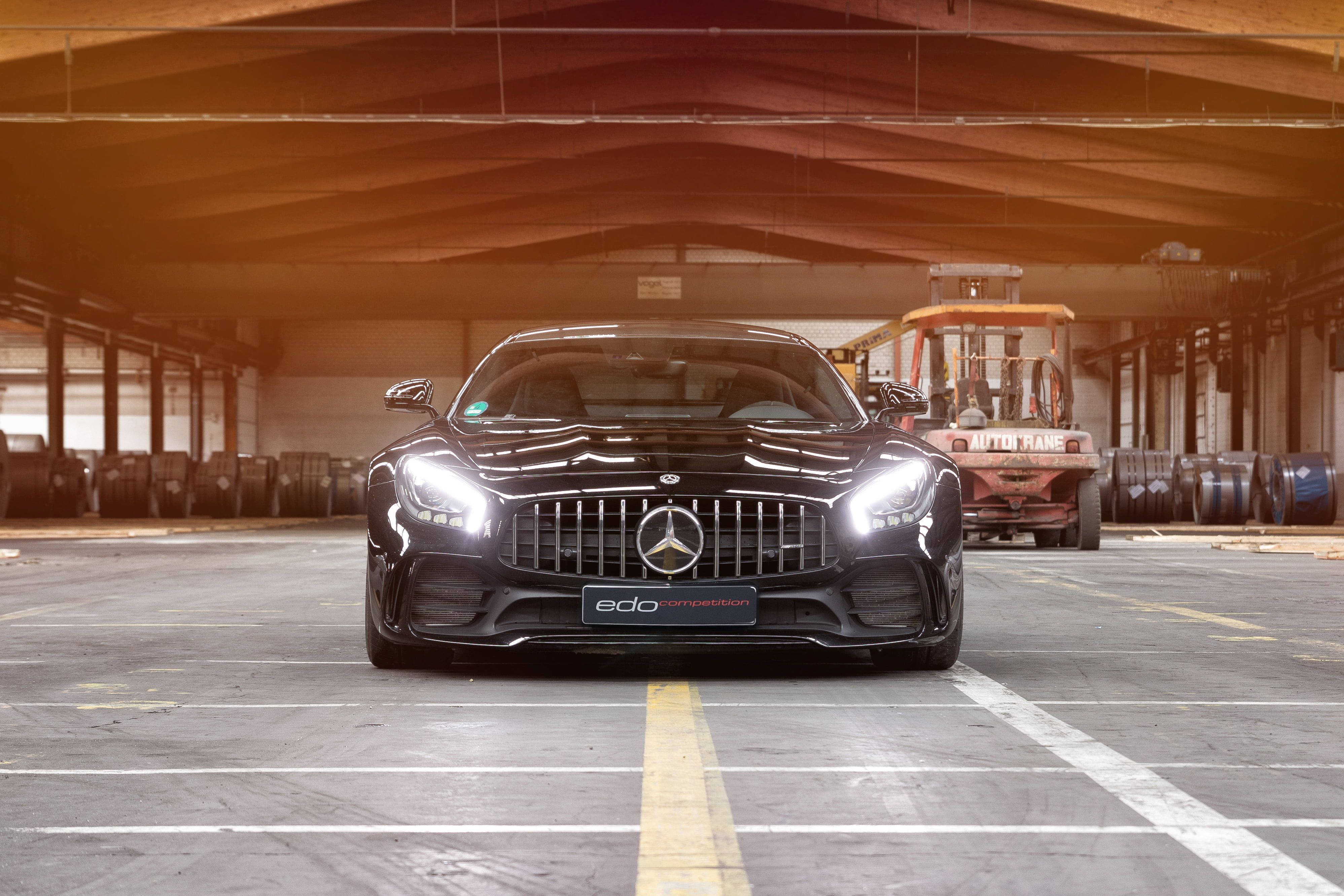 超跑 桌布 壁紙 — 一輛時尚的黑色Mercedes-AMG GT R，配以發光的車頭燈，在溫暖的金色燈光下主宰著寬敞的工業倉庫。
