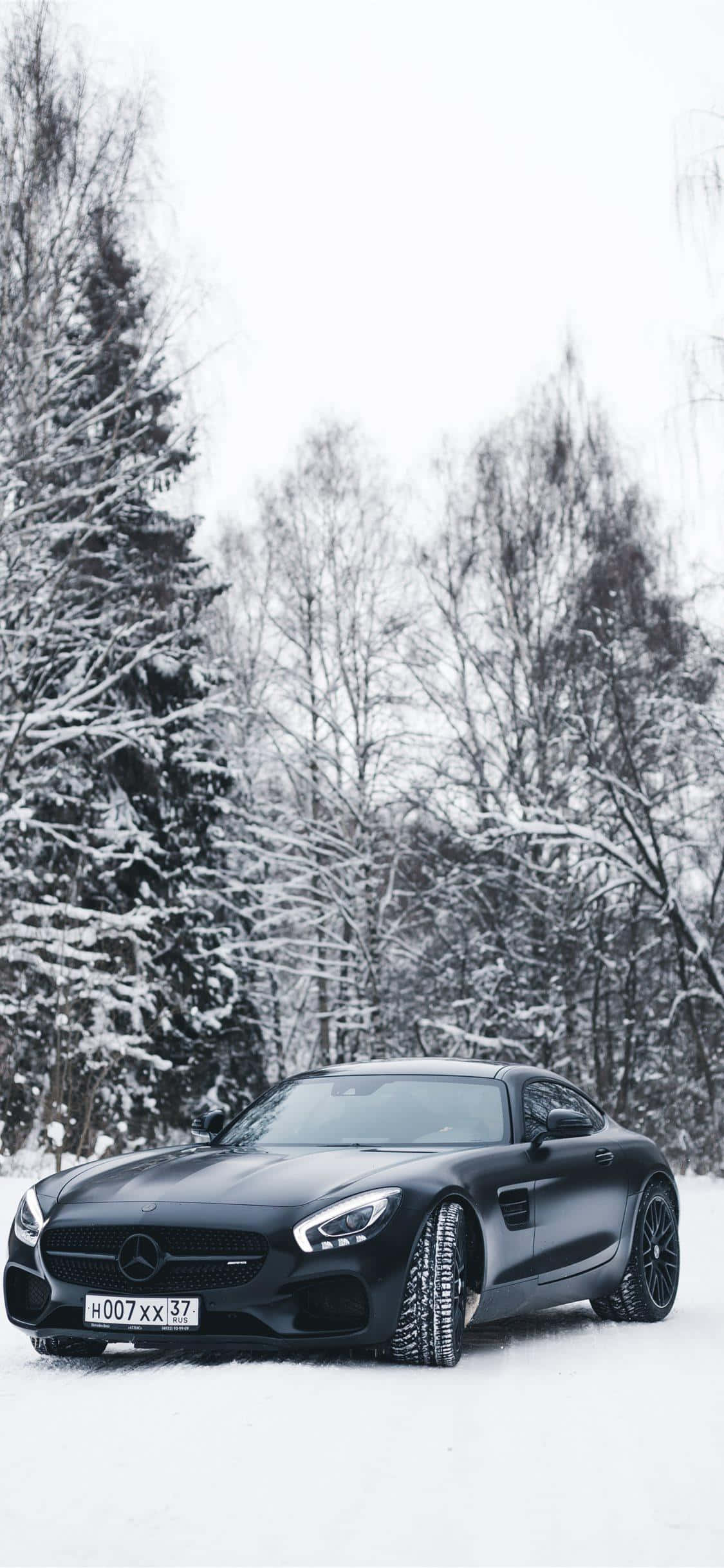 黑色 桌布 壁紙 — 一輛時尚的黑色Mercedes-AMG GT停泊在白雪覆蓋的森林中，雪覆蓋的樹木在陰天之下。