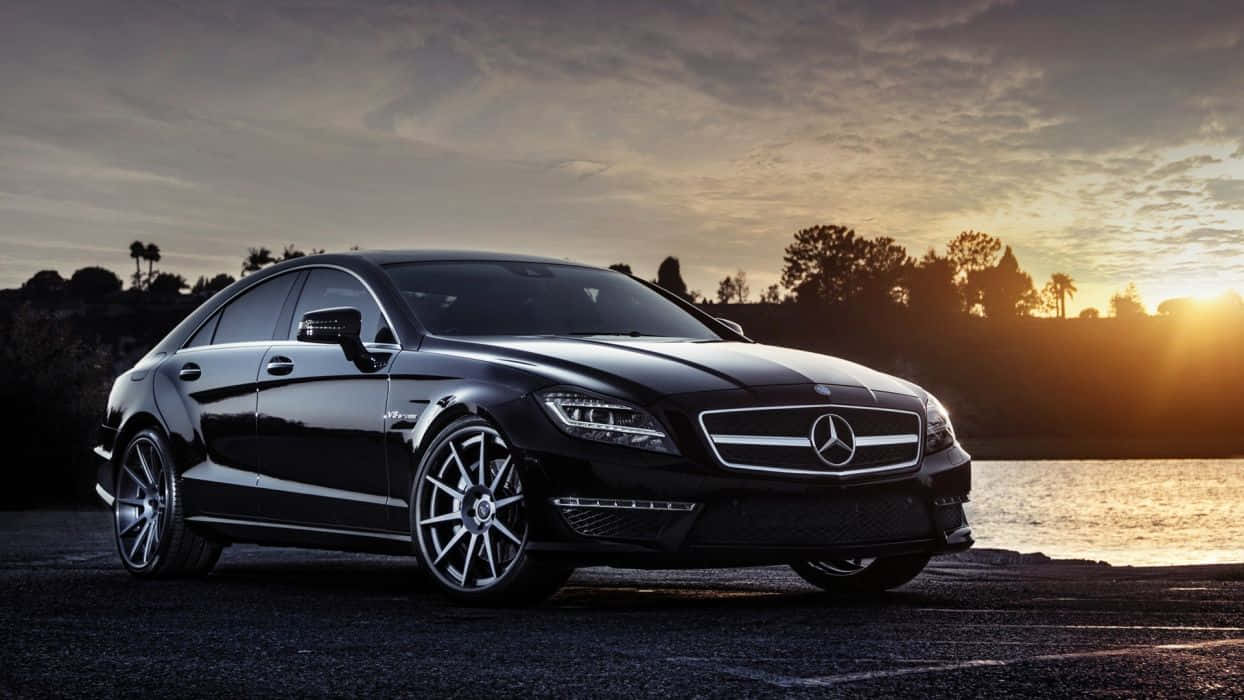 黑色 桌布 壁紙 — 一輛時尚的黑色Mercedes-Benz CLS停在水邊，背景是金色日落和樹木。