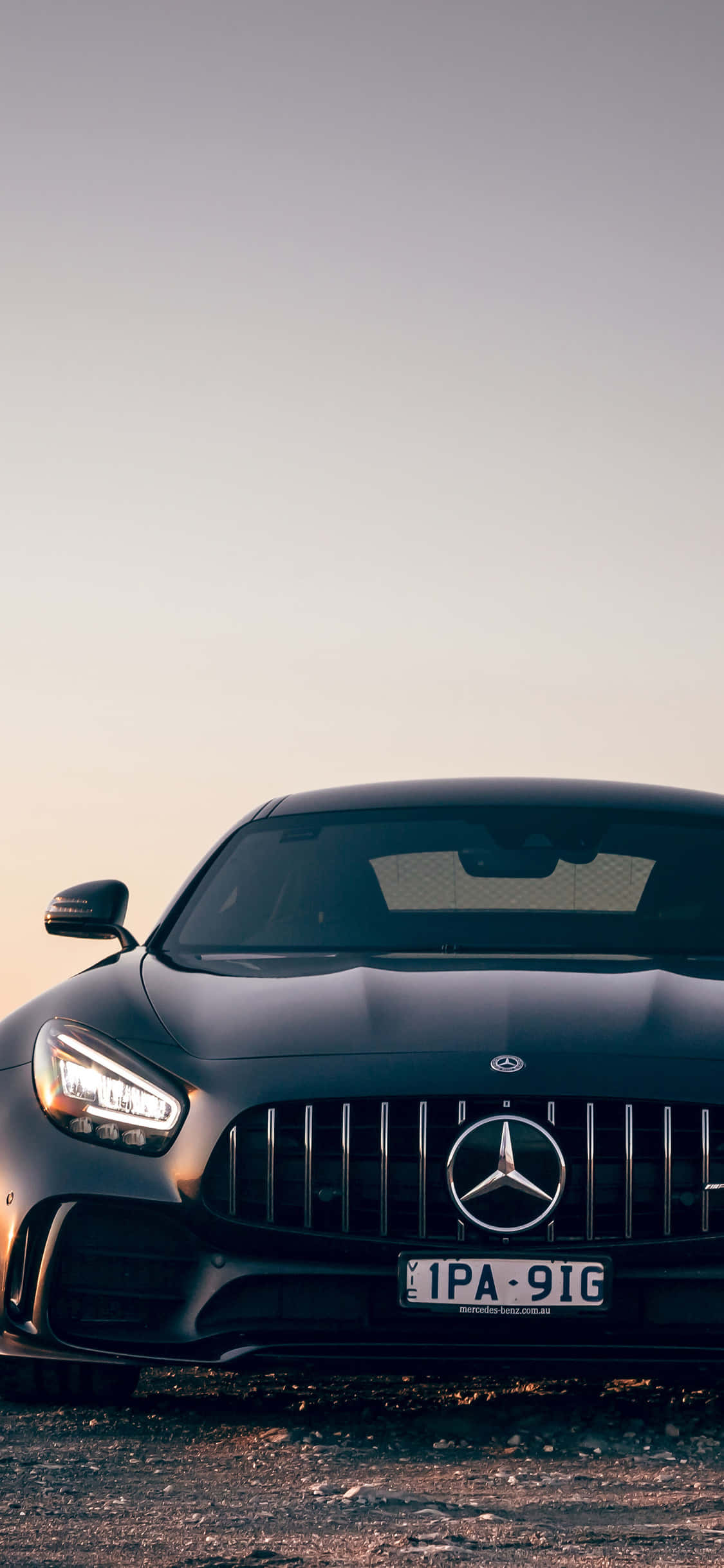 黑色 桌布 壁紙 — 一輛時尚的黑色Mercedes-AMG GT停在碎石上，在柔和暮色天空下，車頭燈閃閃發光。