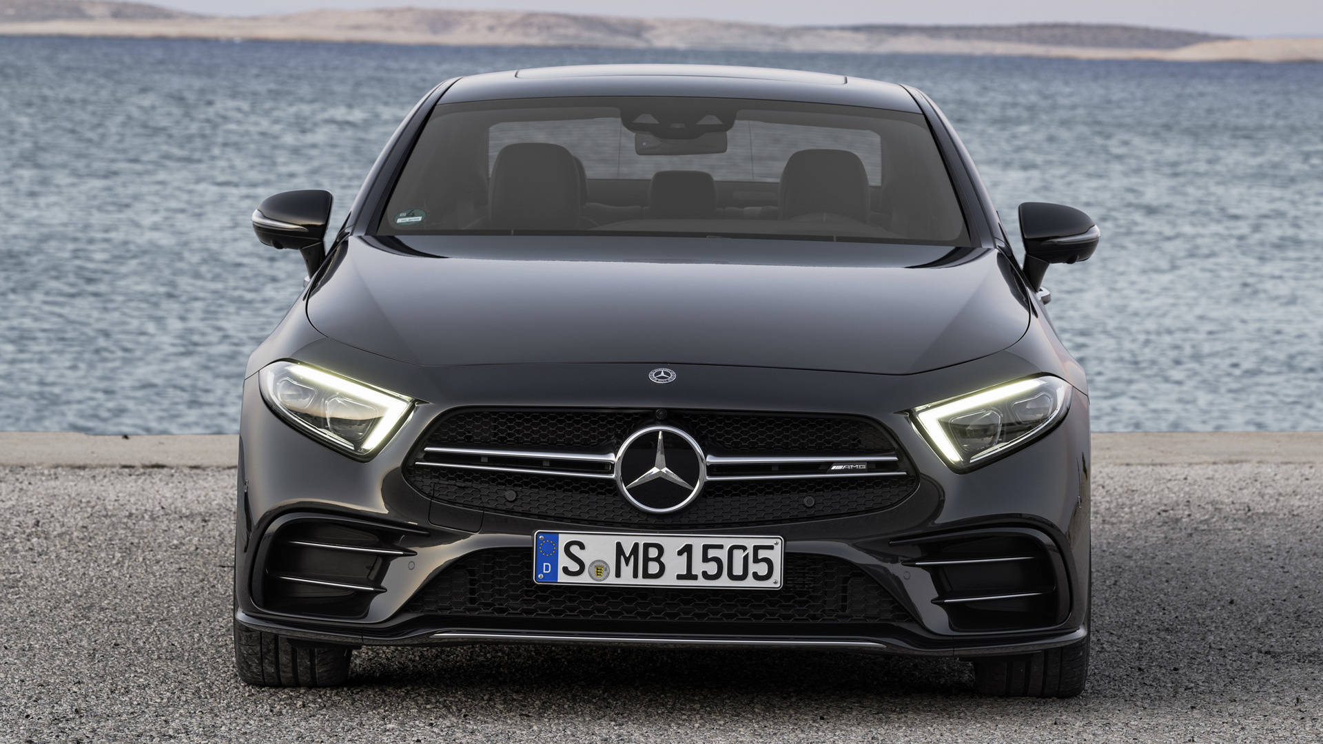 賓士 AMG 桌布 壁紙 — 一輛時尚的黑色Mercedes-AMG A45停放在沿海道路上，背景有海浪。