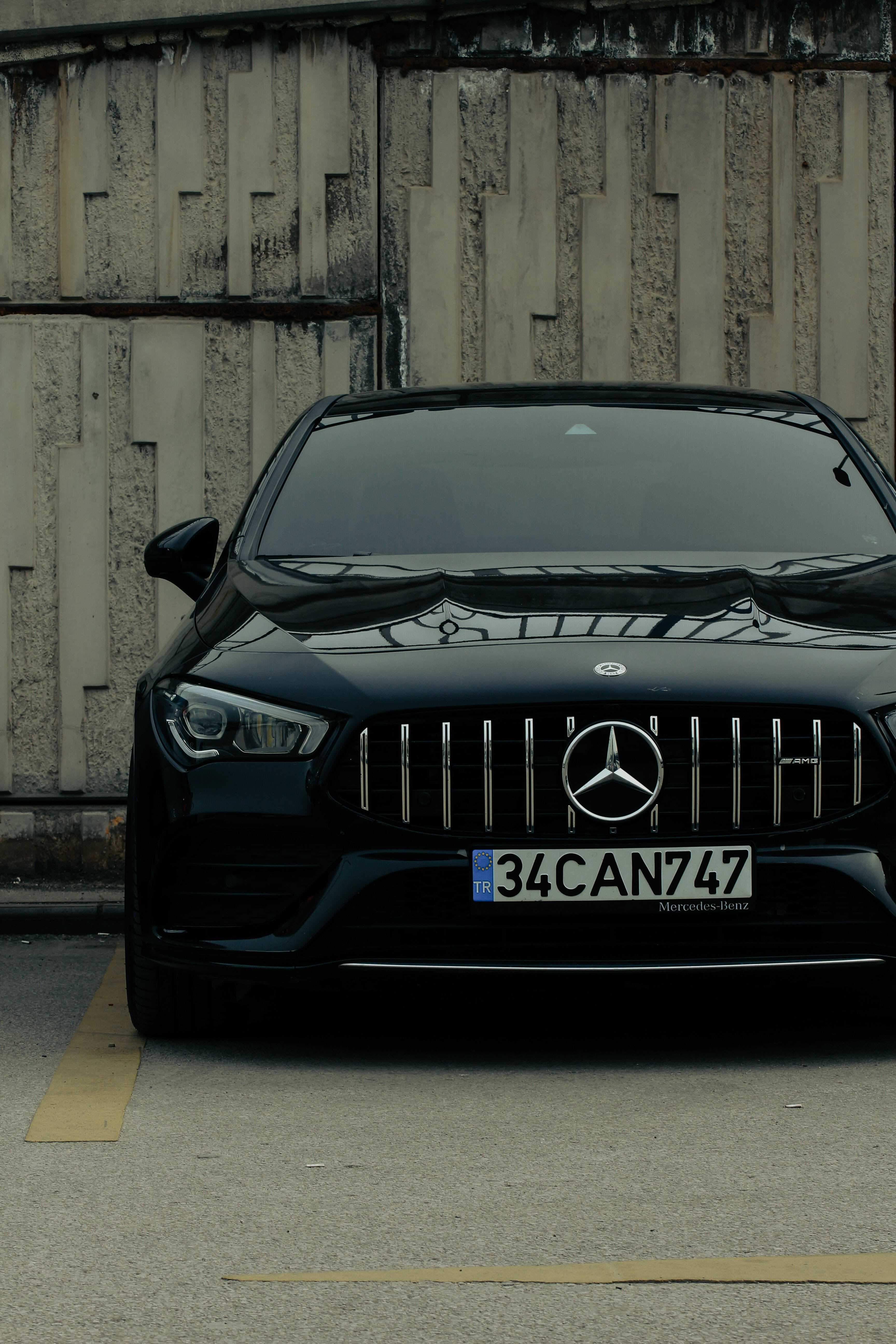 mercedes amg iPhone 桌布 壁紙 — 一輛時尚的黑色Mercedes-AMG停在昏暗燈光下風化的混凝土牆前。