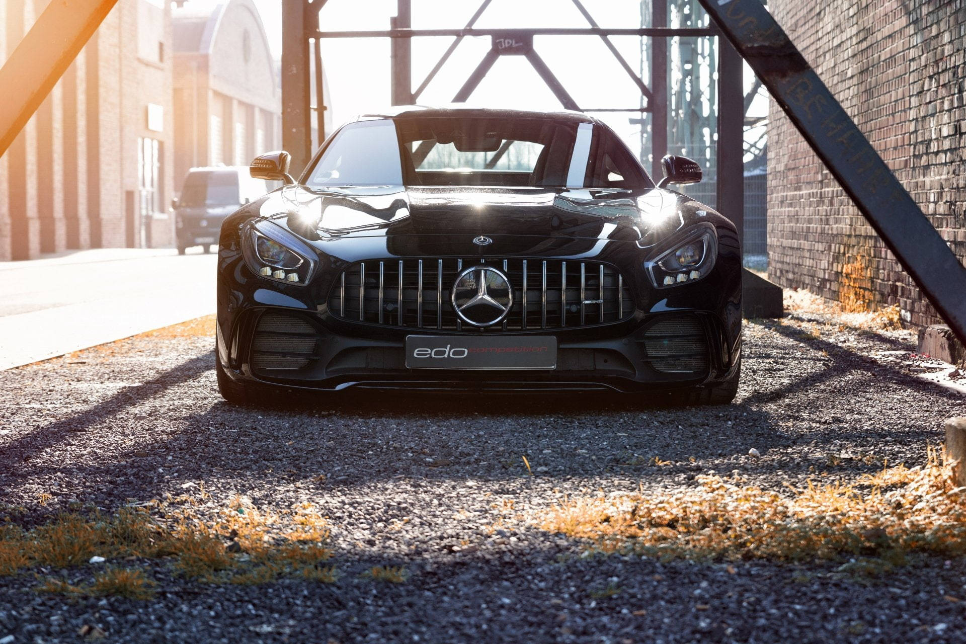 高清 桌布 壁紙 — 一輛時尚的黑色Mercedes-AMG GT停在工業鋼拱門下，金色陽光在礫石上投下長長的影子。