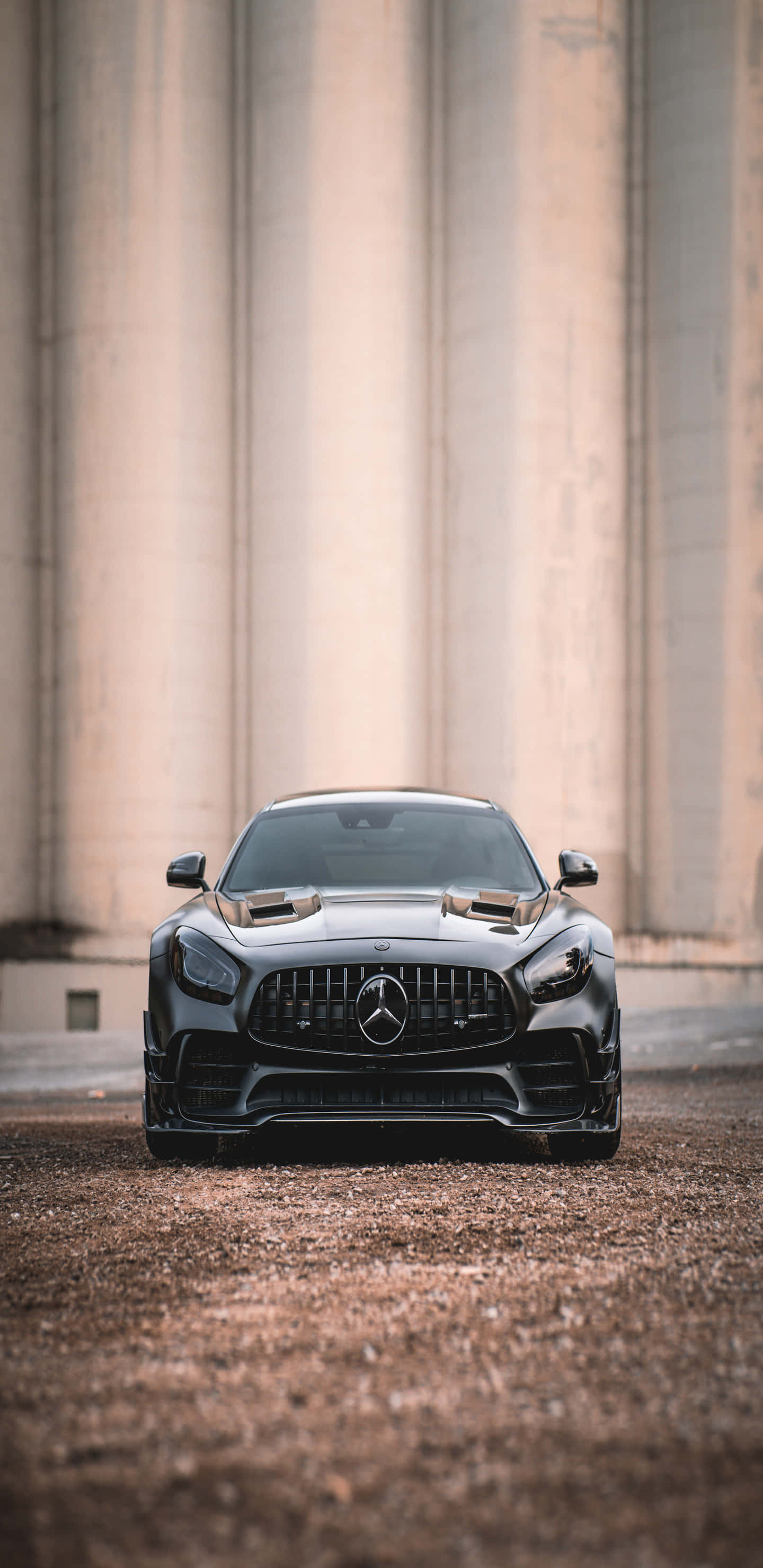 酷車 桌布 壁紙 — 一輛時尚的黑色Mercedes-AMG GT停在碎石上，前方是雄偉的混凝土柱，柔和日光下。