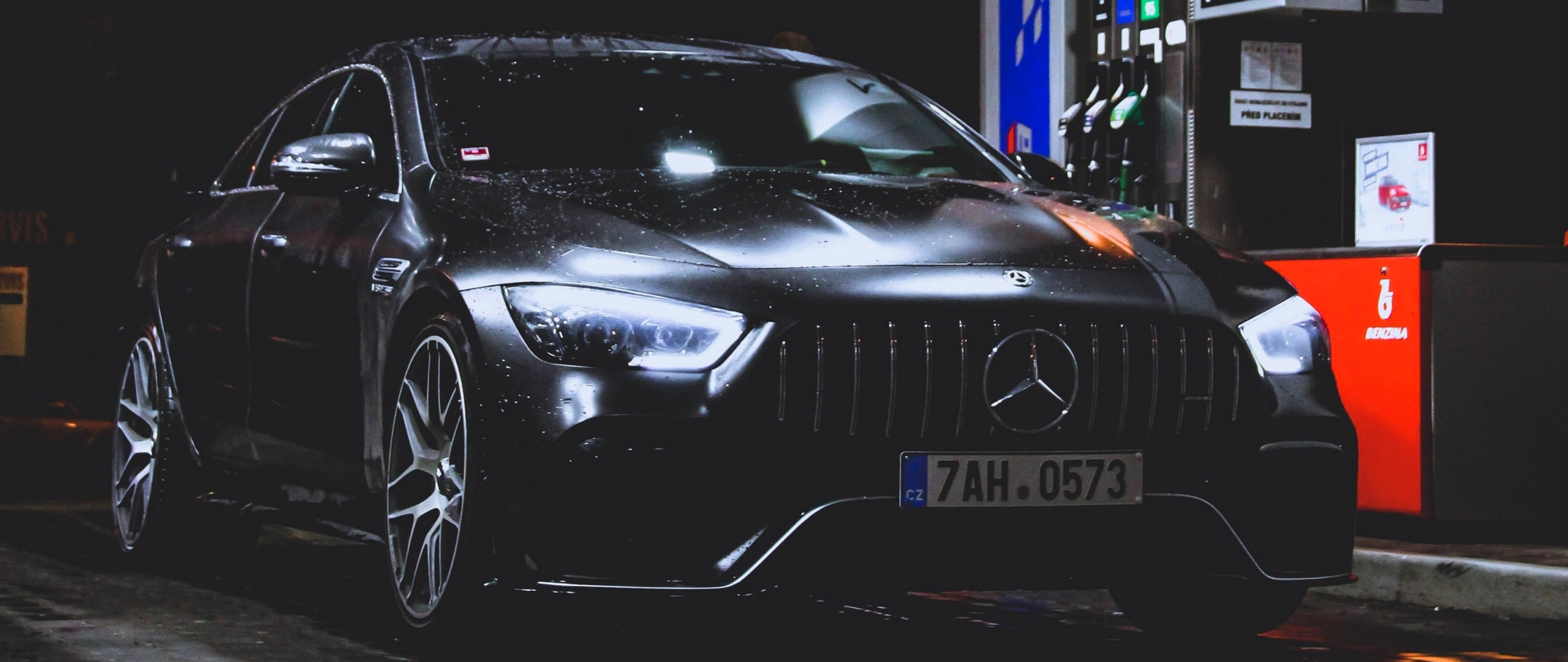4K 奔馳壁紙 桌布 壁紙 — 一輛時尚的黑色Mercedes-AMG在夜間停放在加油站，光滑表面上有雨滴，車頭燈發光。