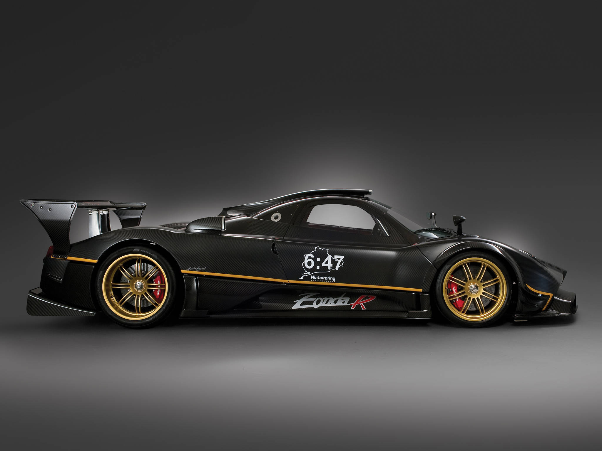 Pagani 桌布 壁紙 — 一輛時尚的黑色Pagani Zonda R賽車，帶有金色裝飾和紅色制動卡鉗，在深色漸變工作室背景前以側面展示。