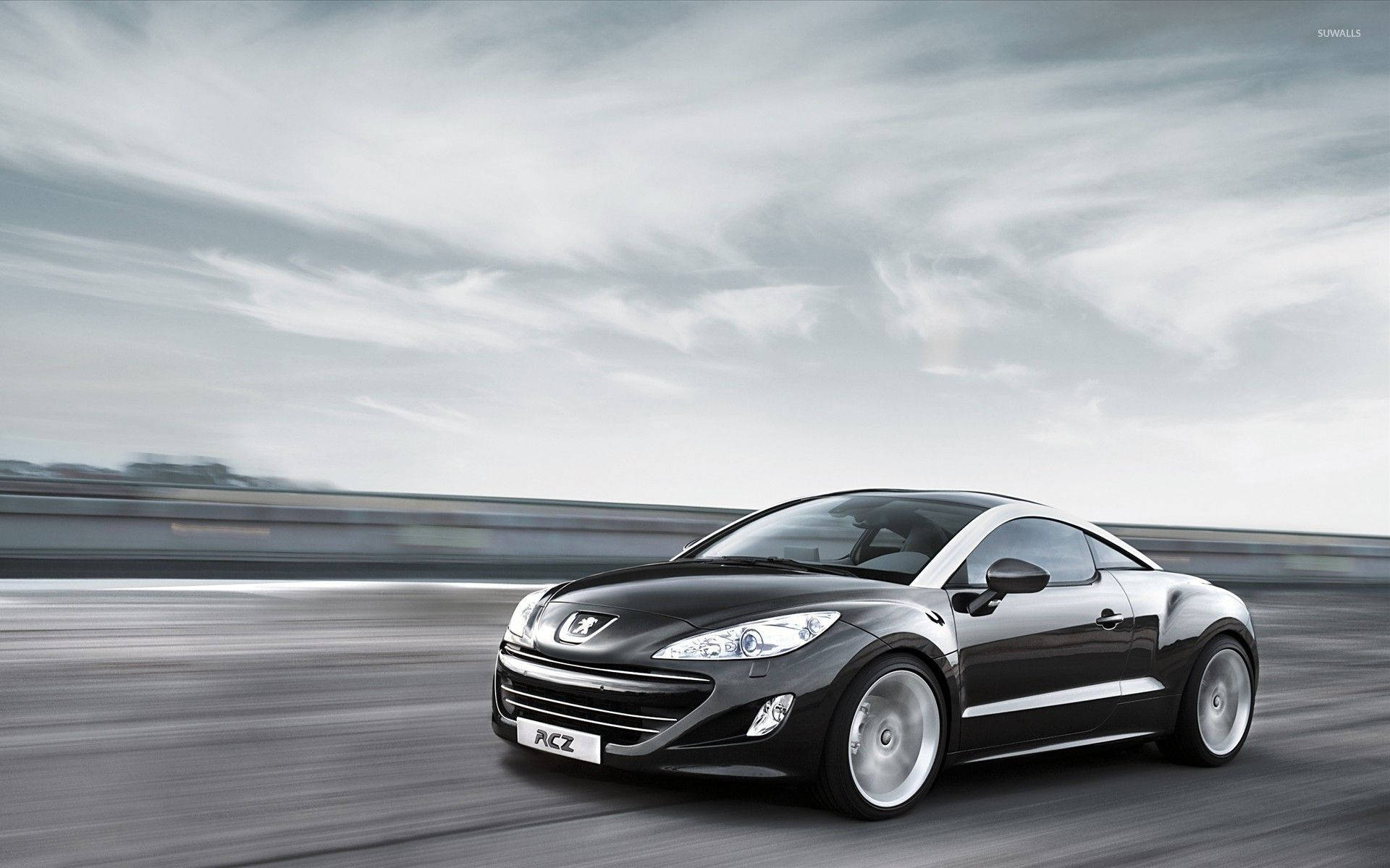Peugeot 桌布 壁紙 — 一輛時尚的黑色Peugeot RCZ跑車在多雲的天空下沿著模糊的高速公路飛馳。