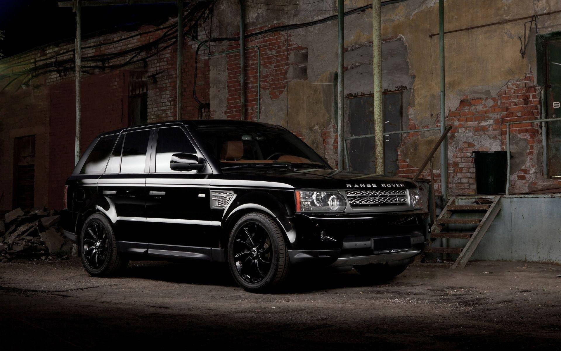 高清 桌布 壁紙 — 一輛時尚的黑色Range Rover SUV停放在光線昏暗的廢棄磚造倉庫中，周圍有外露管道和生鏽的金屬樓梯。