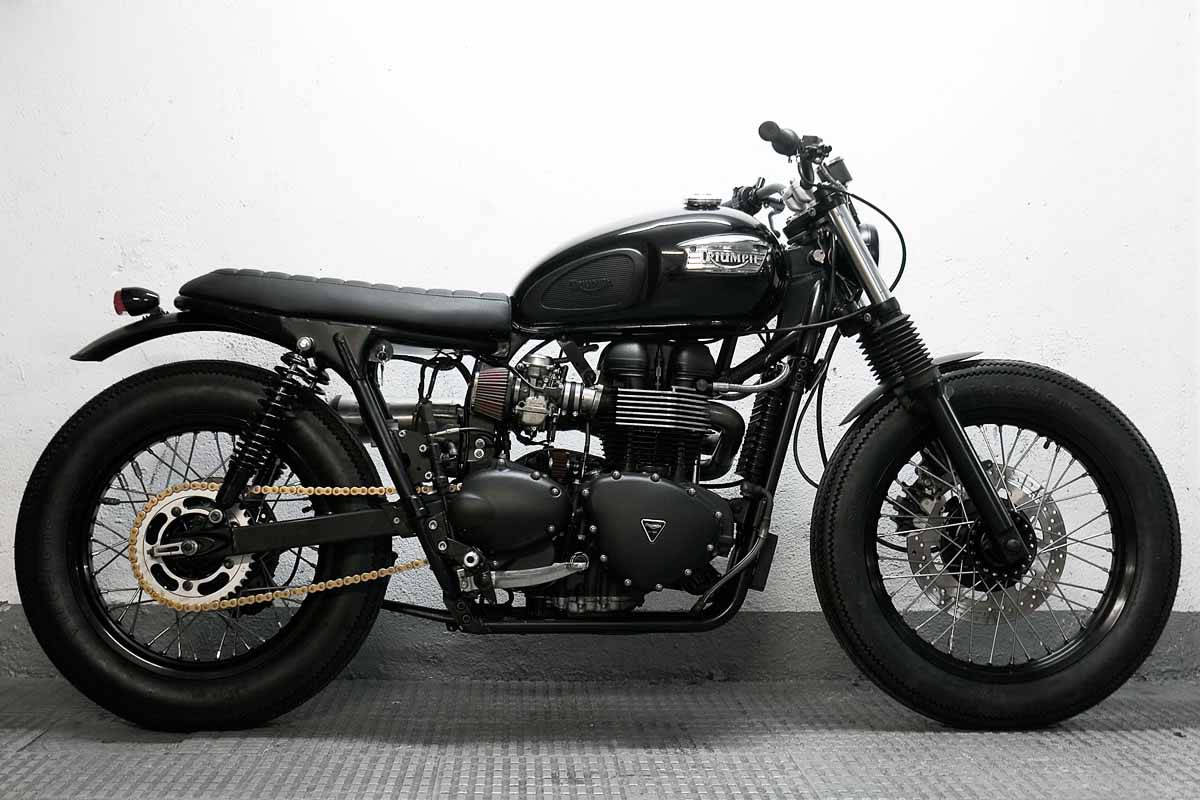 Triumph 桌布 壁紙 — 一輛時尚的黑色Triumph摩托車，帶有鍍鉻裝飾和厚輪胎，在紋理地板上對著白色牆壁擺好姿勢。
