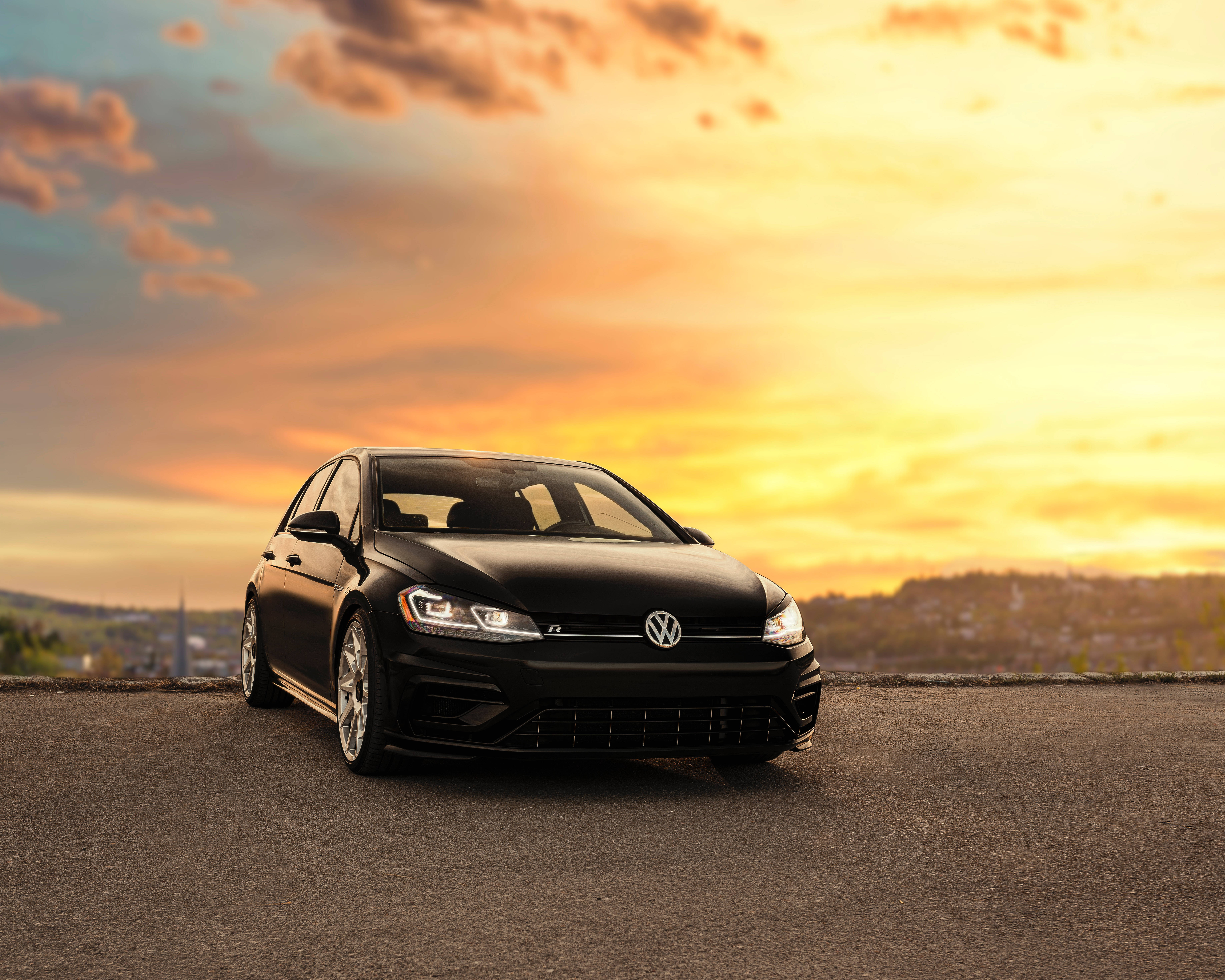 福斯汽車 桌布 壁紙 — 一輛時尚的黑色Volkswagen Golf R停在日落時分的道路上，伴隨著溫暖的金色雲彩和遠山。