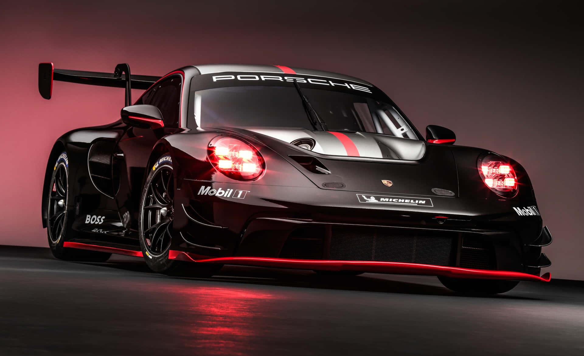 PORSCHE 911 壁紙 — 一輛時尚的黑色保時捷賽車，帶有發光的紅色頭燈和裝飾，矗立在粉紅色和灰色的漸變工作室背景前。