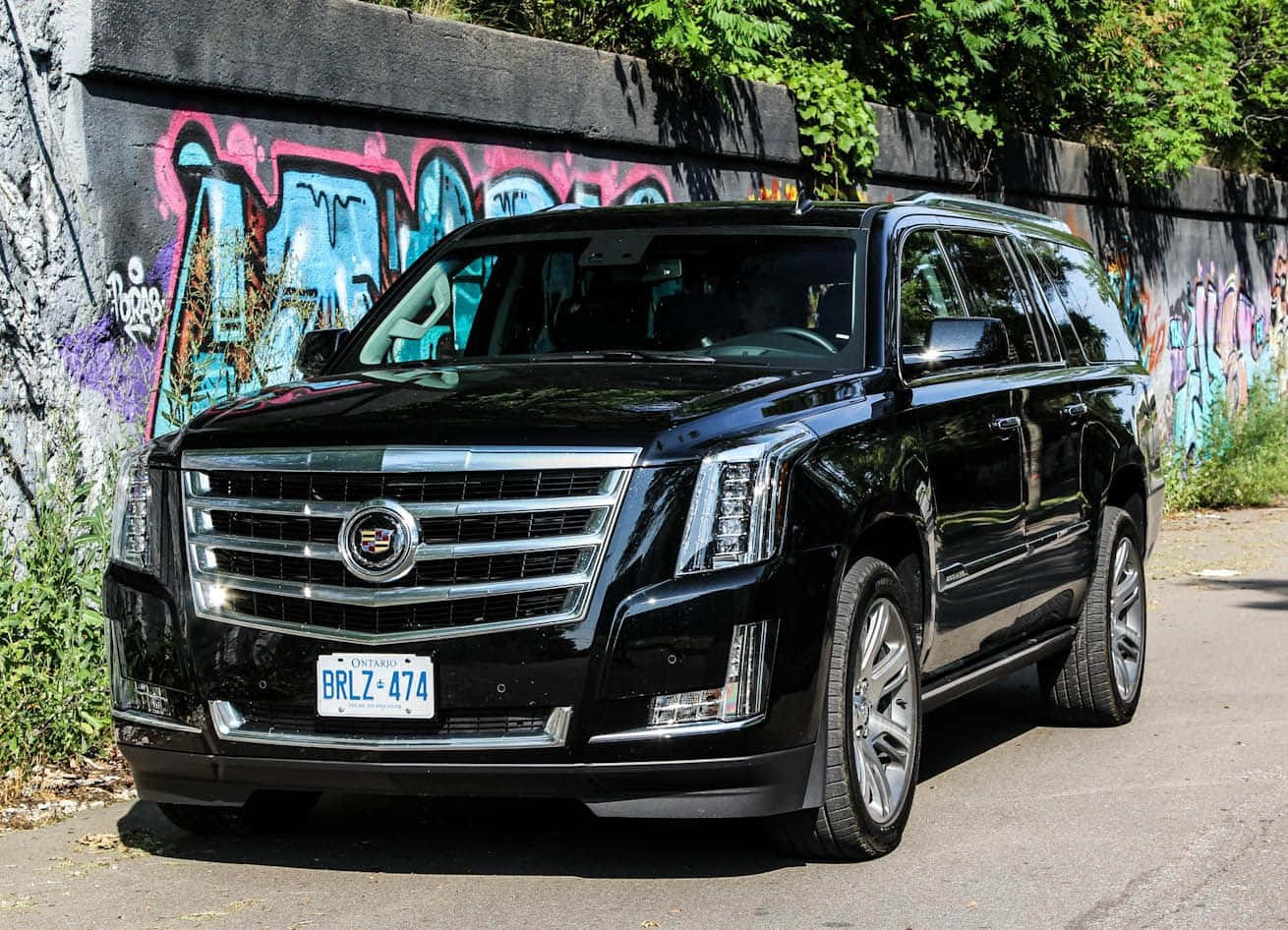 Cadillac Escalade 桌布 壁紙 — 一輛時尚的黑色凱迪拉克凱雷德停在充滿活力的塗鴉牆旁，在明亮的日光下。