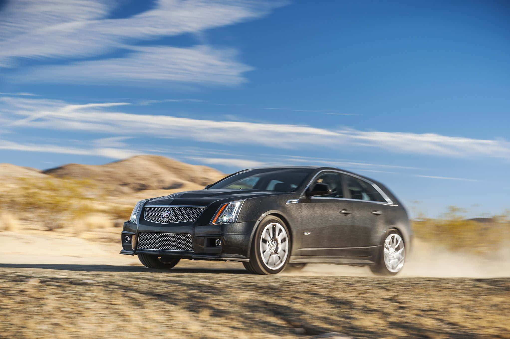 Cadillac Cts 桌布 壁紙 — 一輛時尚的黑色凱迪拉克轎車在塵土飛揚的沙漠公路上疾馳，天空湛藍，白雲輕飄。