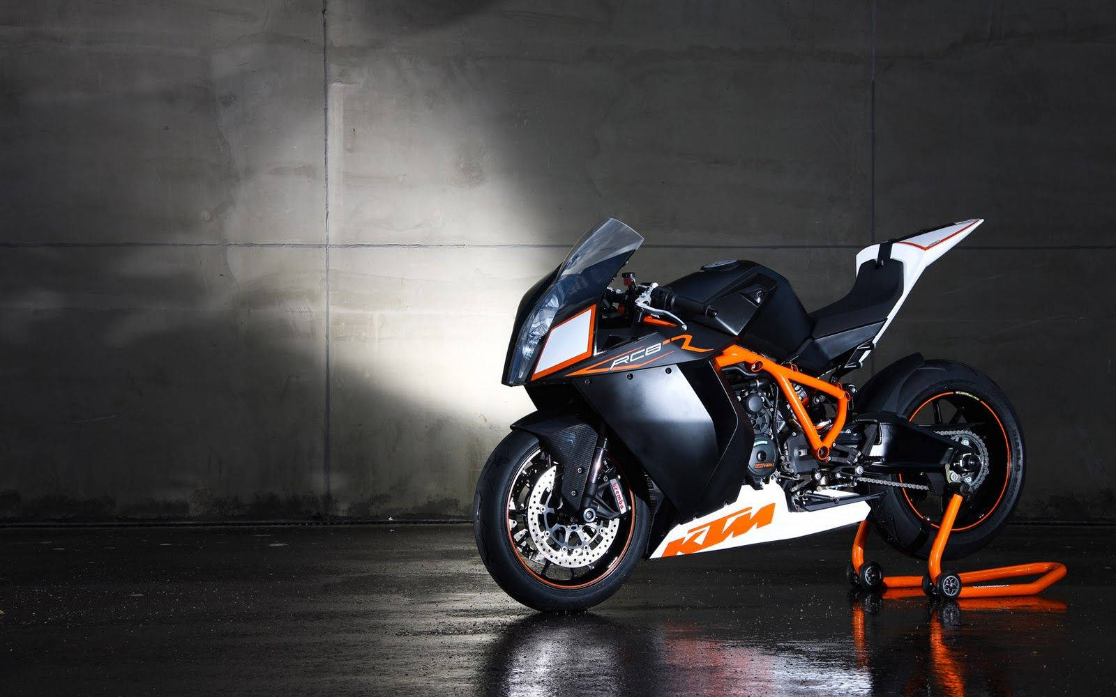 腳踏車 桌布 壁紙 — 一輛時尚的黑色和橙色KTM RC8R摩托車在工作室環境中，戲劇性地照亮在濕混凝土牆前。