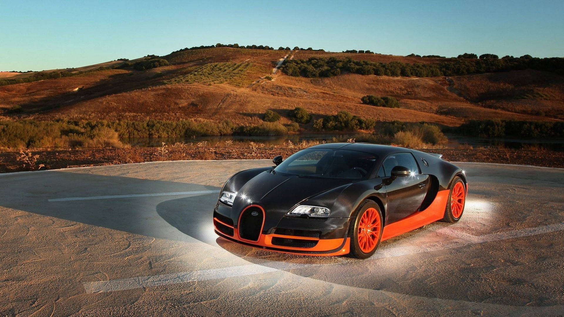 Cool Bugatti 桌布 壁紙 — 一輛時尚的黑色和橙色布加迪威龍停泊在彎曲的道路上，背景是金色山丘和清澈的藍天。