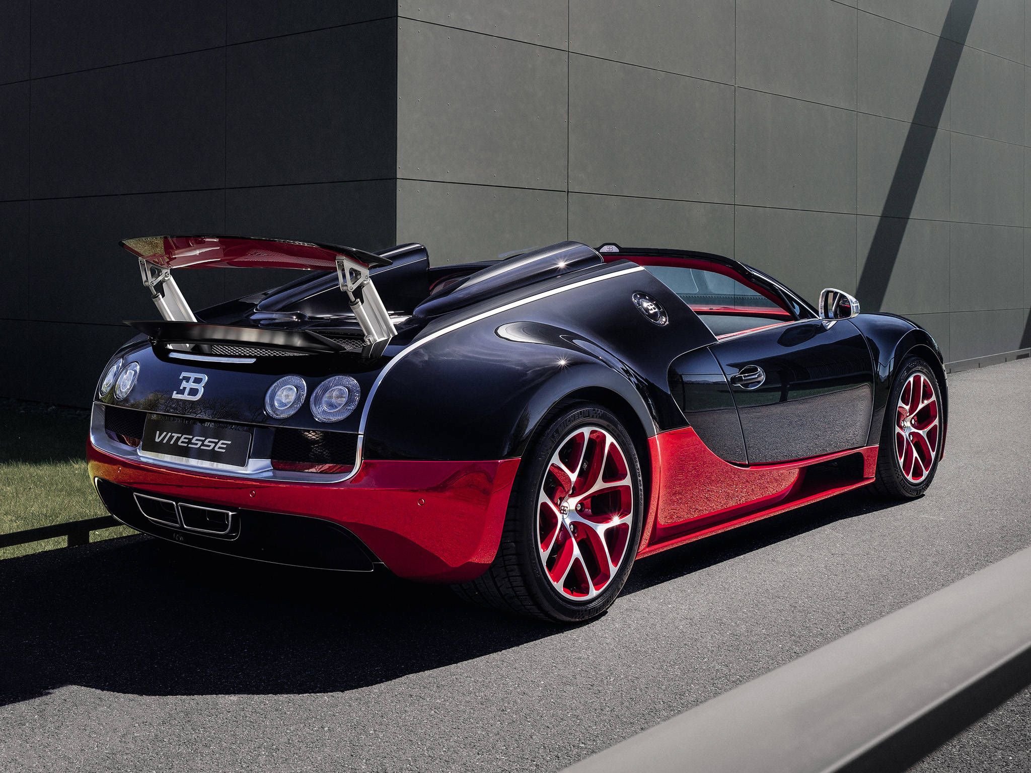 bugatti iPhone 桌布 壁紙 — 一輛時尚的黑色和紅色Bugatti Vitesse超級跑車在明亮的陽光下停靠在現代灰色牆壁旁。