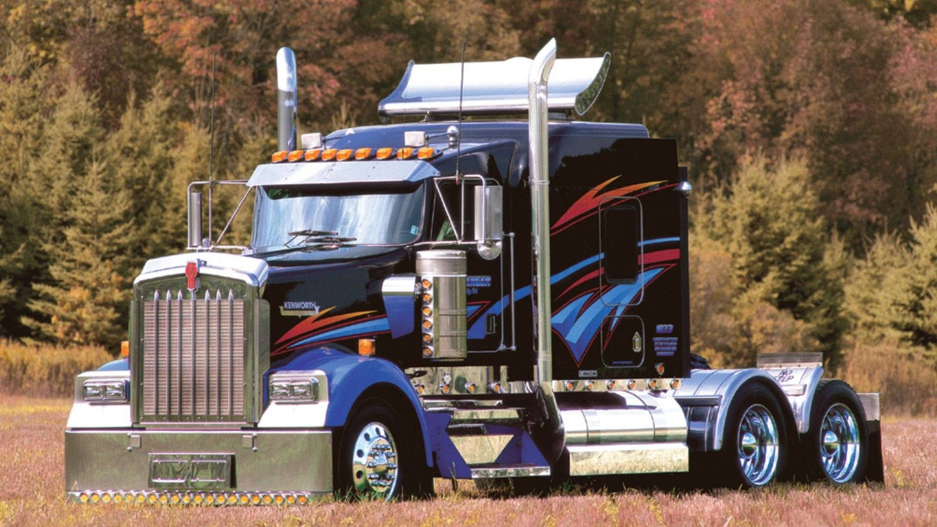 Kenworth 桌布 壁紙 — 一輛時尚的黑色和藍色 Kenworth 半掛卡車，帶有鍍鉻裝飾和火焰貼花，自豪地站在秋葉田野中。