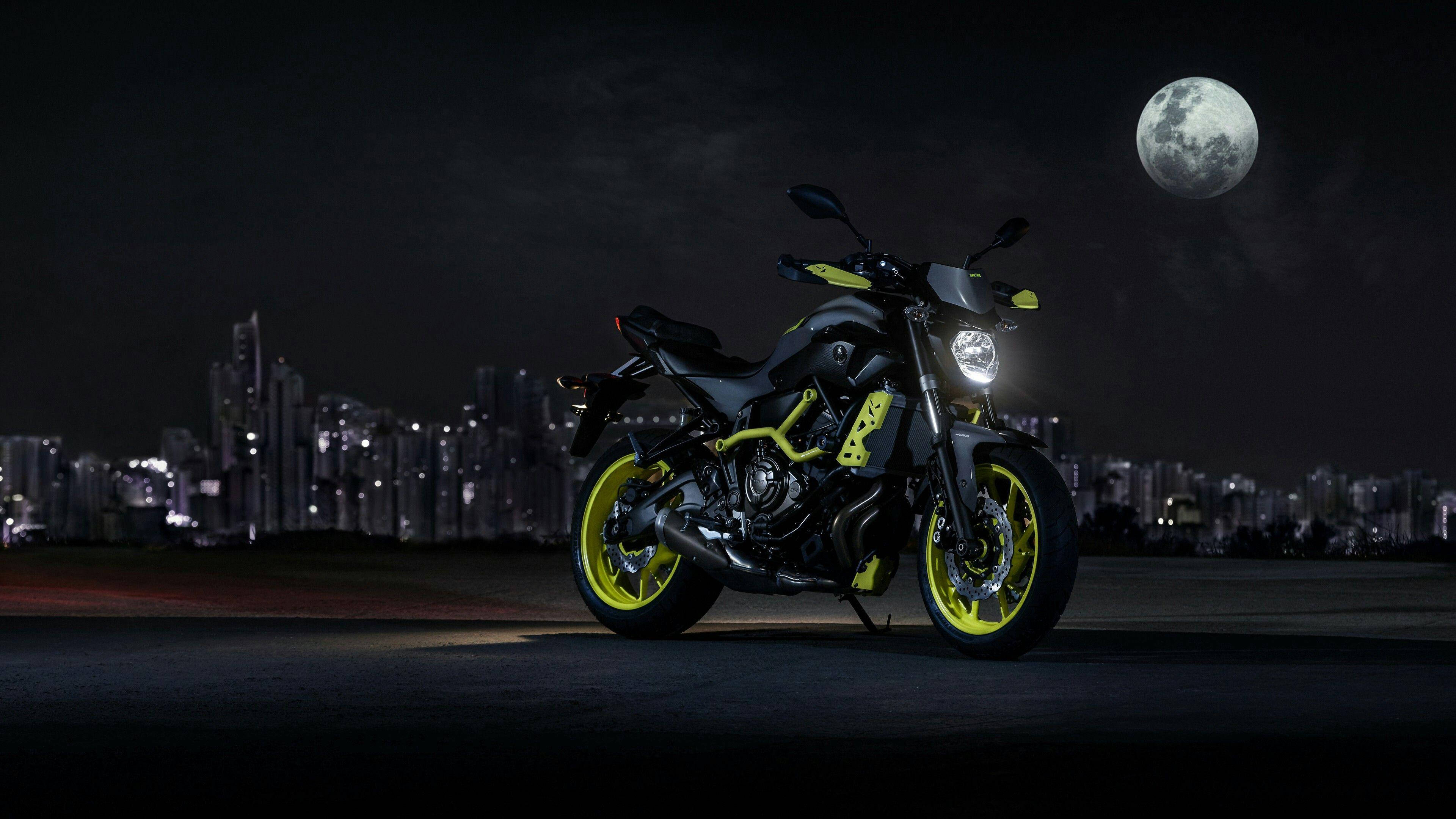 yamaha mt 15 桌布 壁紙 — 一輛時尚的黑色和螢光黃色機車在滿月下閃耀，背景是夜晚發光的城市天際線。