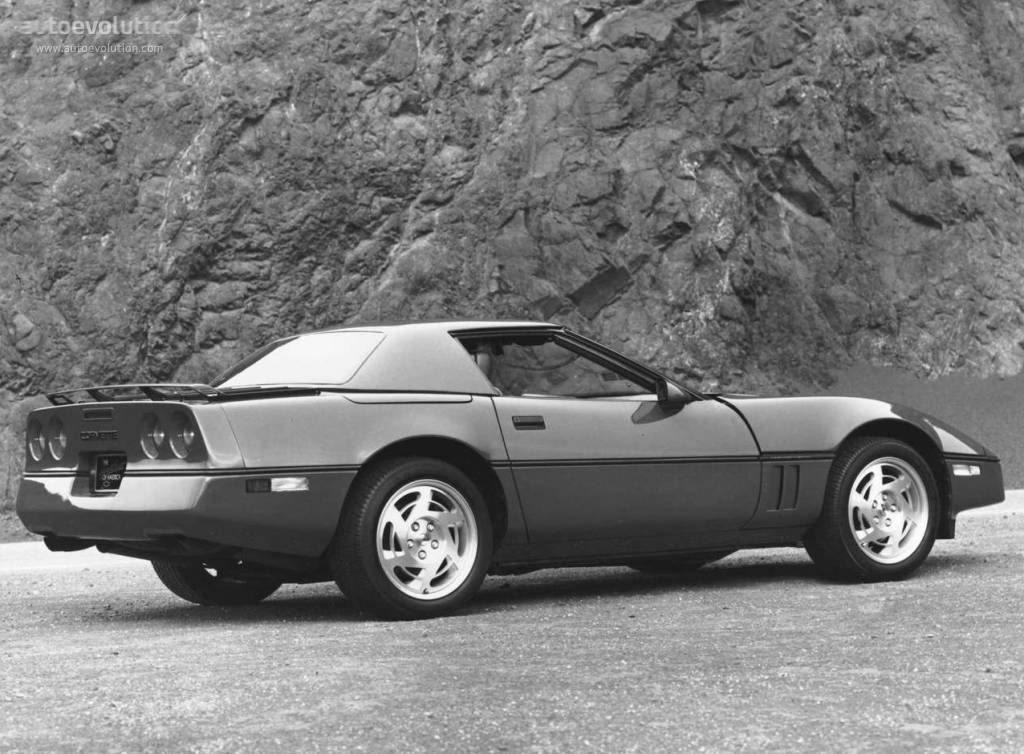 corvette 桌布 壁紙 — 一輛時尚的黑色和銀色敞篷跑車停泊在碎石上，背景是單色的崎嶇岩石懸崖面。