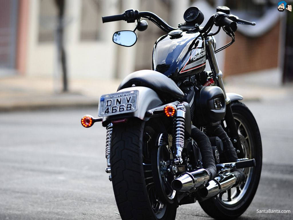Harley 桌布 壁紙 — 一輛時尚的黑色哈雷戴維森摩托車停在城市街道上，帶有鍍鉻裝飾和發光的尾燈。