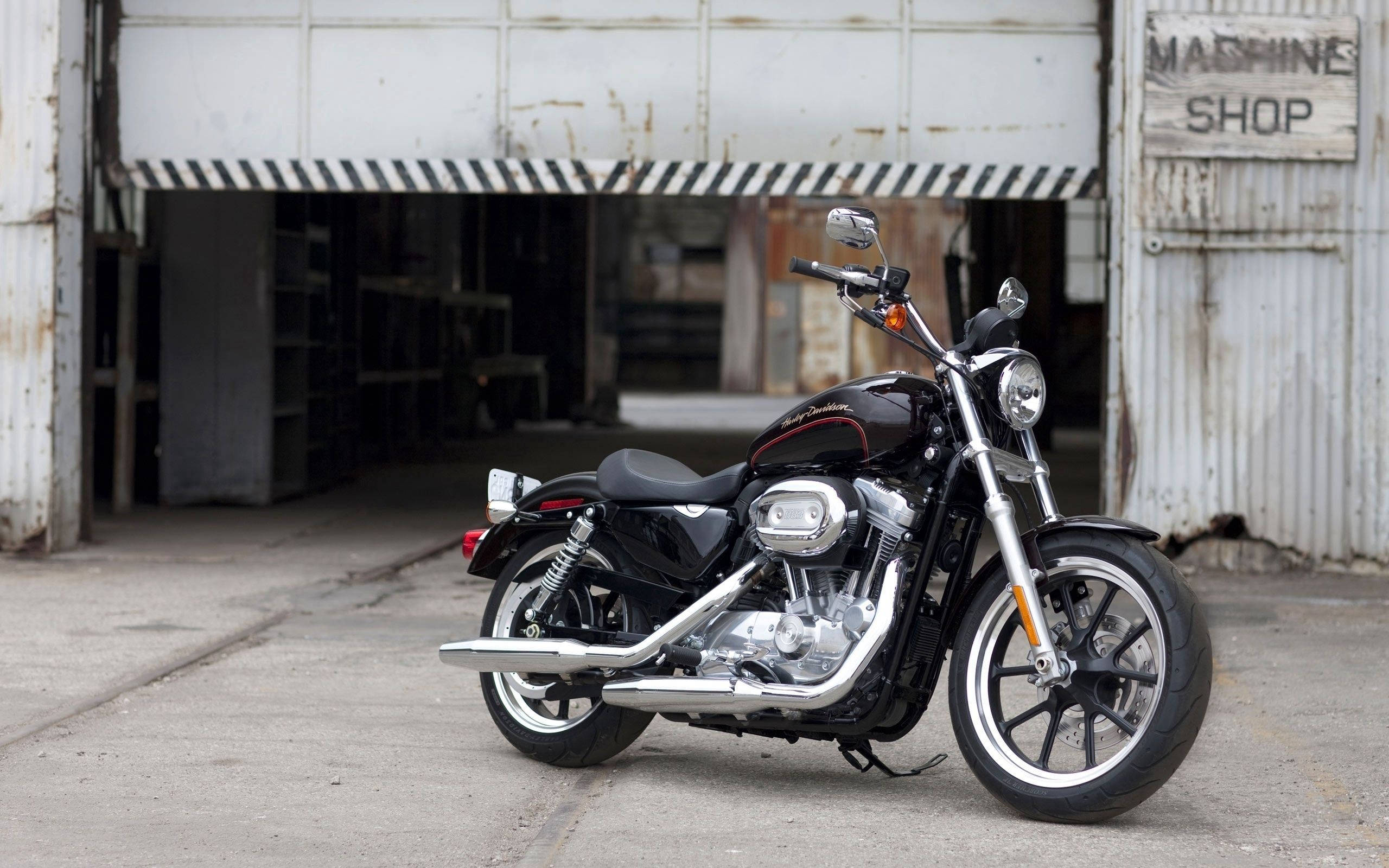 Harley 桌布 壁紙 — 一輛時尚的黑色哈雷機車停在風化的機器工廠門前，門上有剝落的油漆和條紋遮陽篷。