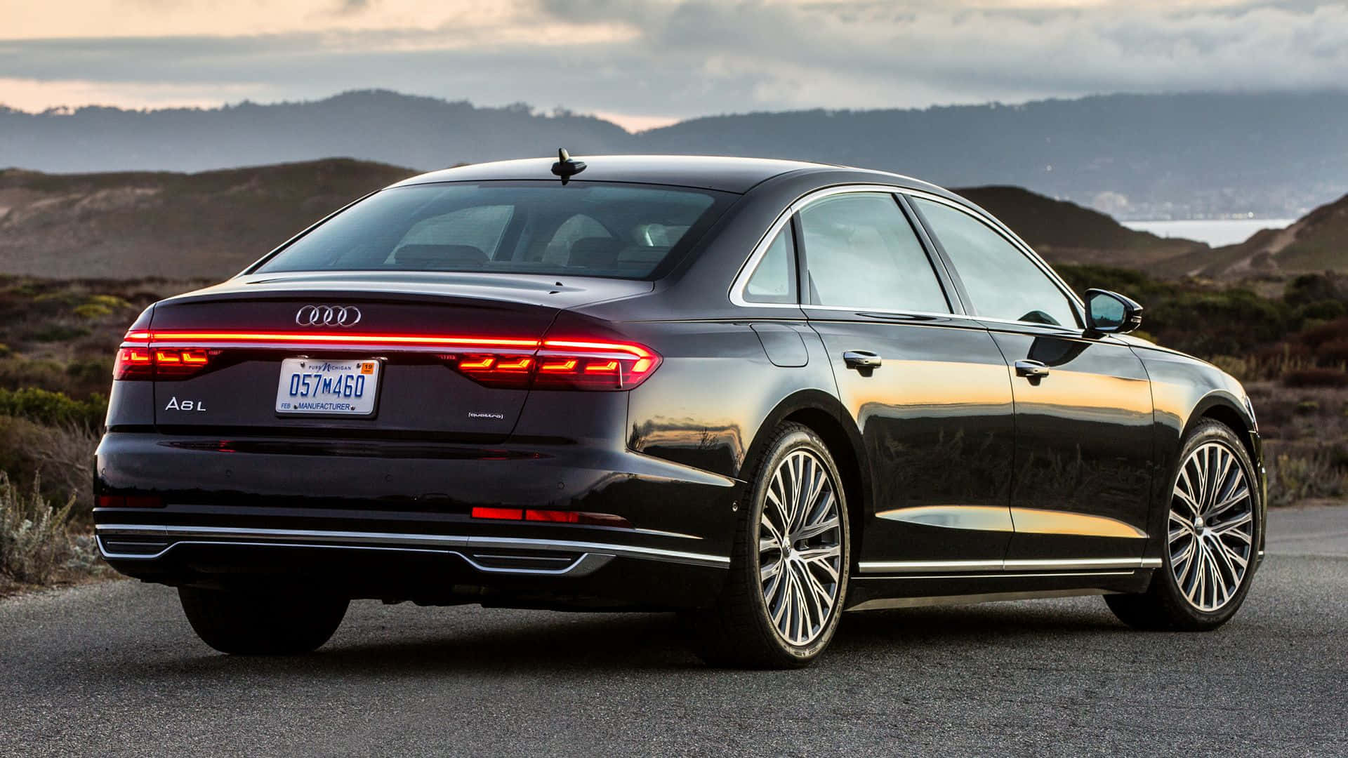 Audi S8 桌布 壁紙 — 一輛時尚的黑色奧迪A8 L轎車停在日落時分的沿海公路上，背景是山丘和海洋。