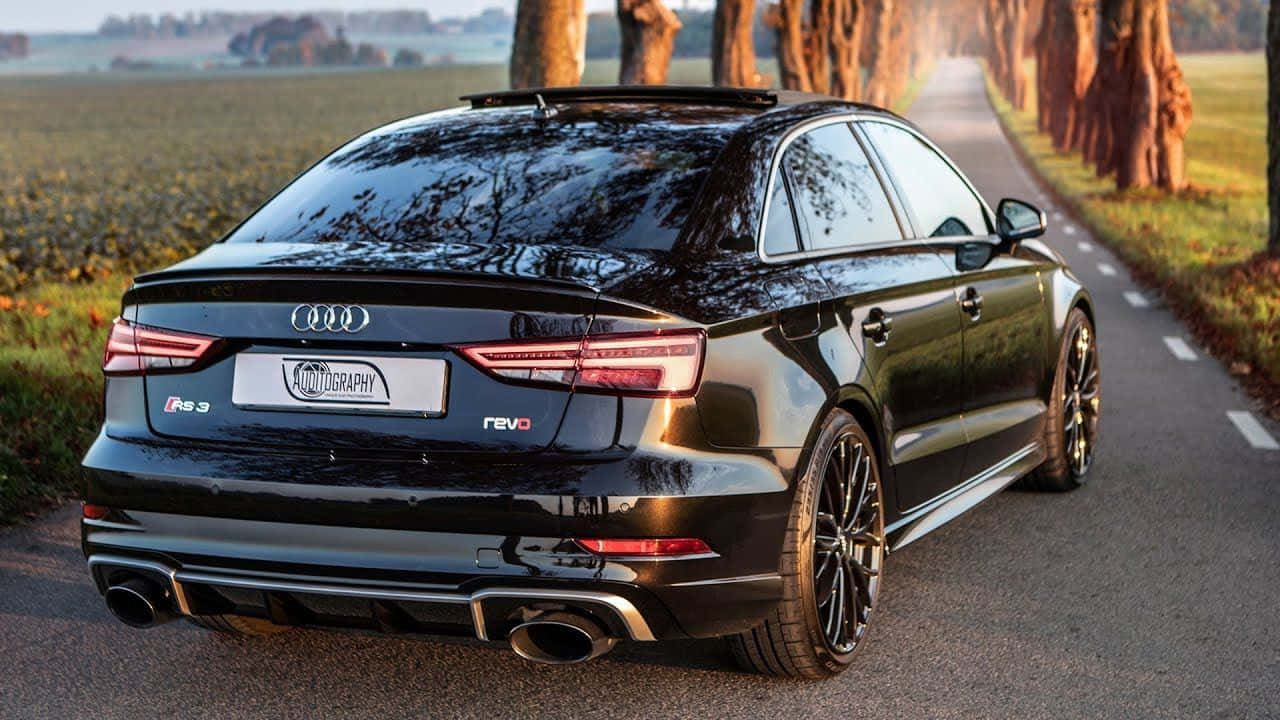 Sedan 桌布 壁紙 — 一輛時尚的黑色奧迪RS3轎車在金色黃昏光線下行駛在綠樹成蔭的鄉村道路上，閃閃發光。