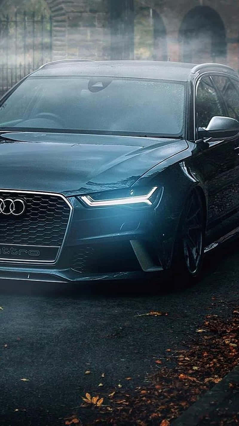 Audi iPhone 桌布 壁紙 — 一輛時尚的黑色奧迪RS6停放在濕漉漉的馬路上，路面散落著秋天的落葉，籠罩在薄霧暮色中。