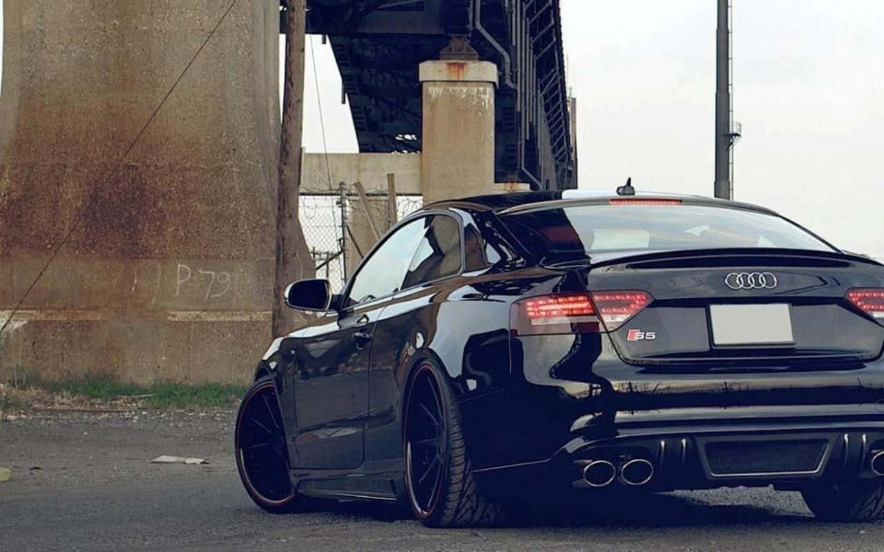 Audi S5 桌布 壁紙 — 一輛時尚的黑色奧迪S5雙門轎跑車停在生鏽的橋下，混凝土柱上有塗鴉。