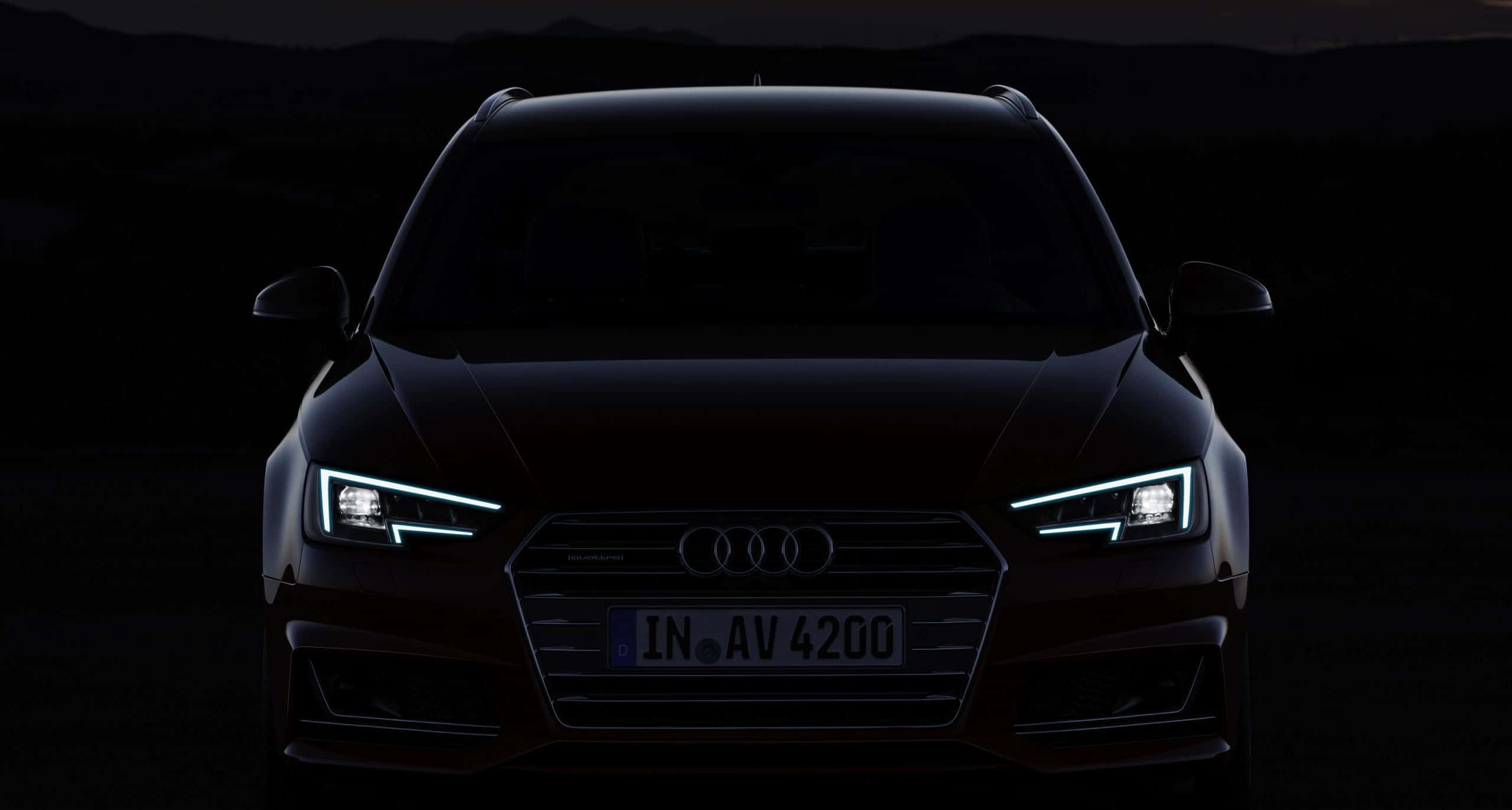 Audi A4 桌布 壁紙 — 一輛時尚的黑色奧迪SUV，在黃昏時分被發光的車頭燈照亮，背景是黑暗的山巒。