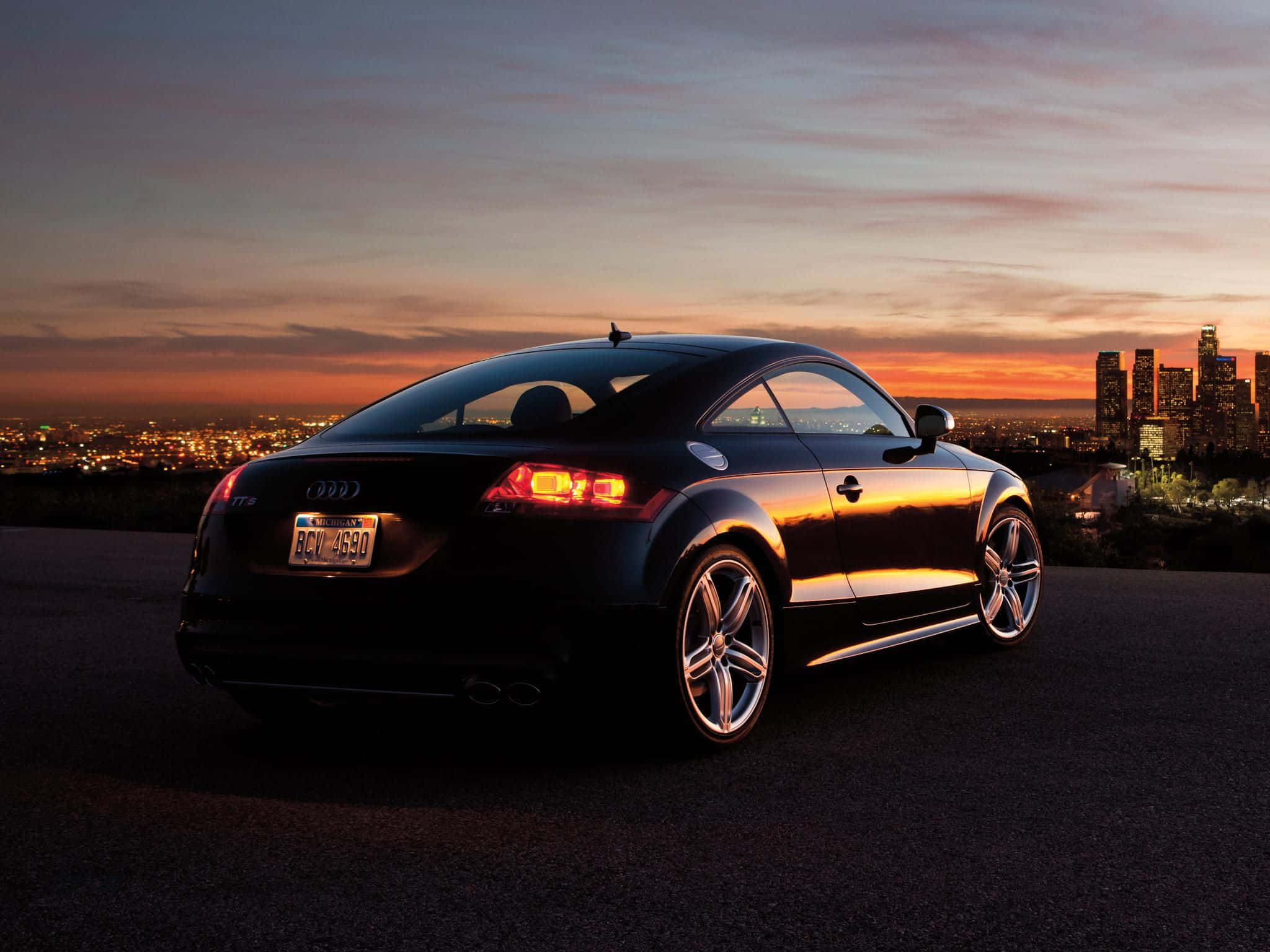 Audi Tt 桌布 壁紙 — 一輛時尚的黑色奧迪TT雙門轎跑車在夕陽色調下閃閃發光，遠處是廣闊的城市天際線。