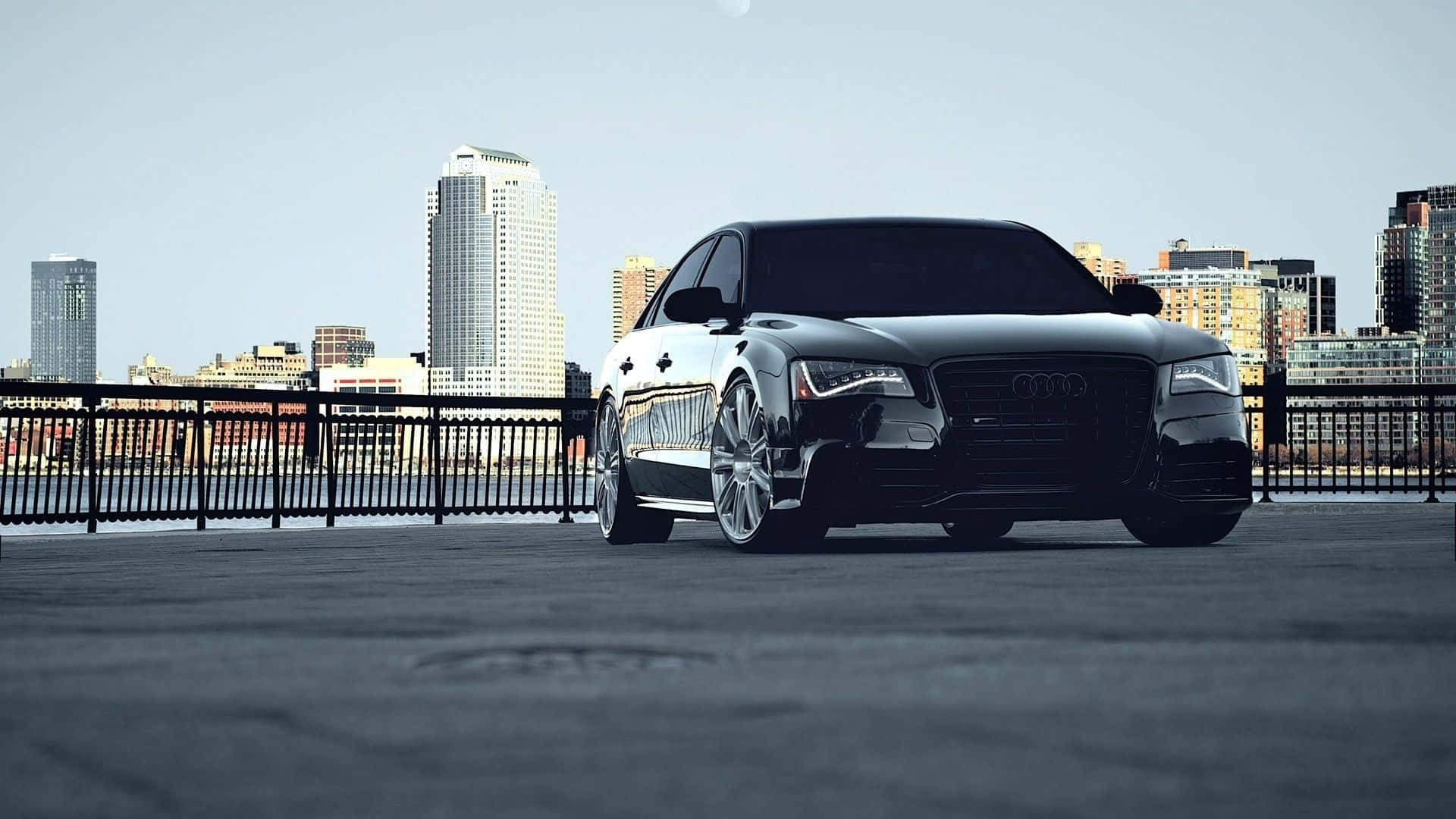 Audi S8 桌布 壁紙 — 一輛時尚的黑色奧迪房車停放在城市屋頂，背景是現代化的天際線，天空晴朗。