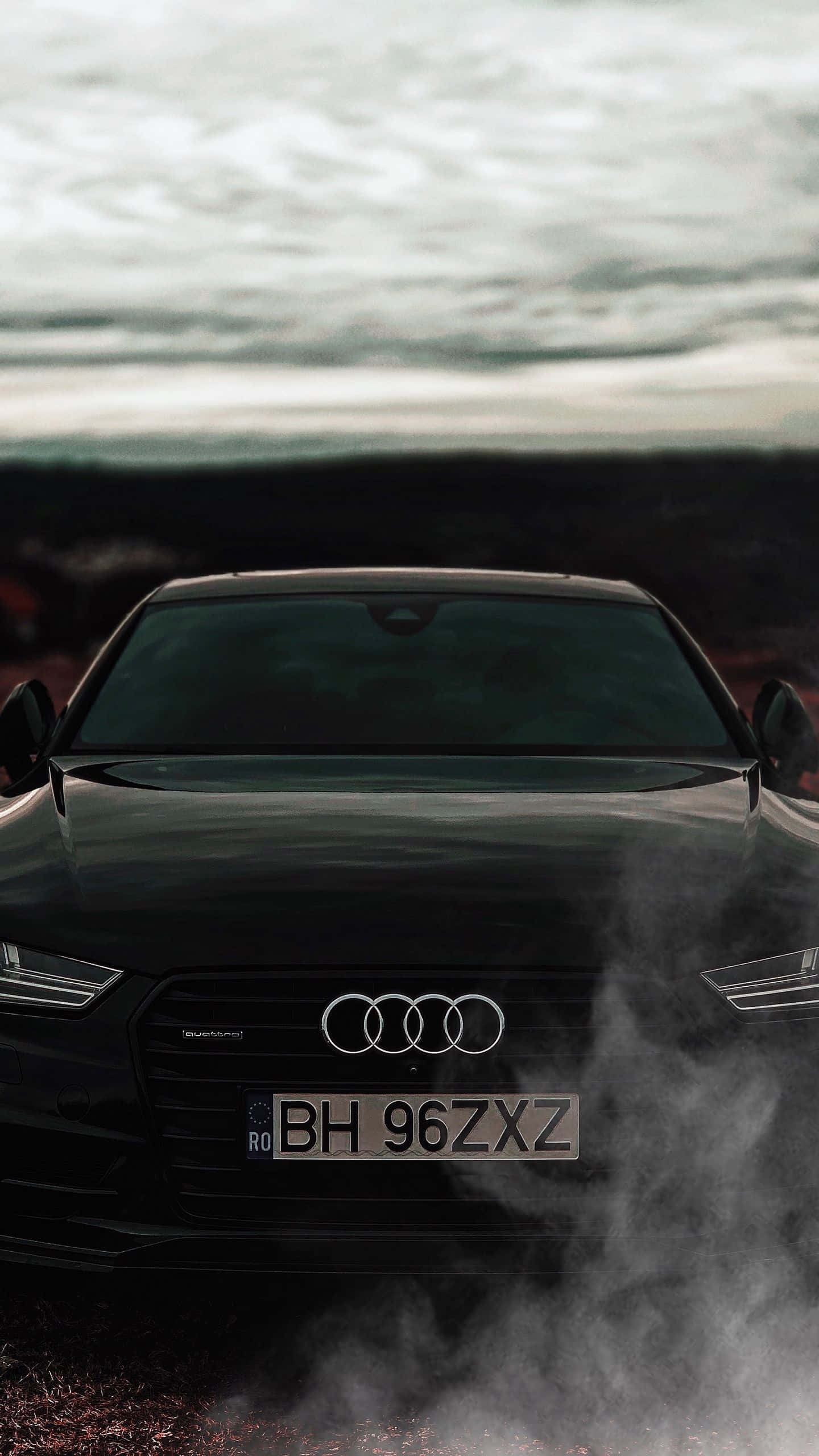 Audi S7 桌布 壁紙 — 一輛時尚的黑色奧迪汽車，車頭冒煙，背景是陰沉的陰天和模糊的風景。