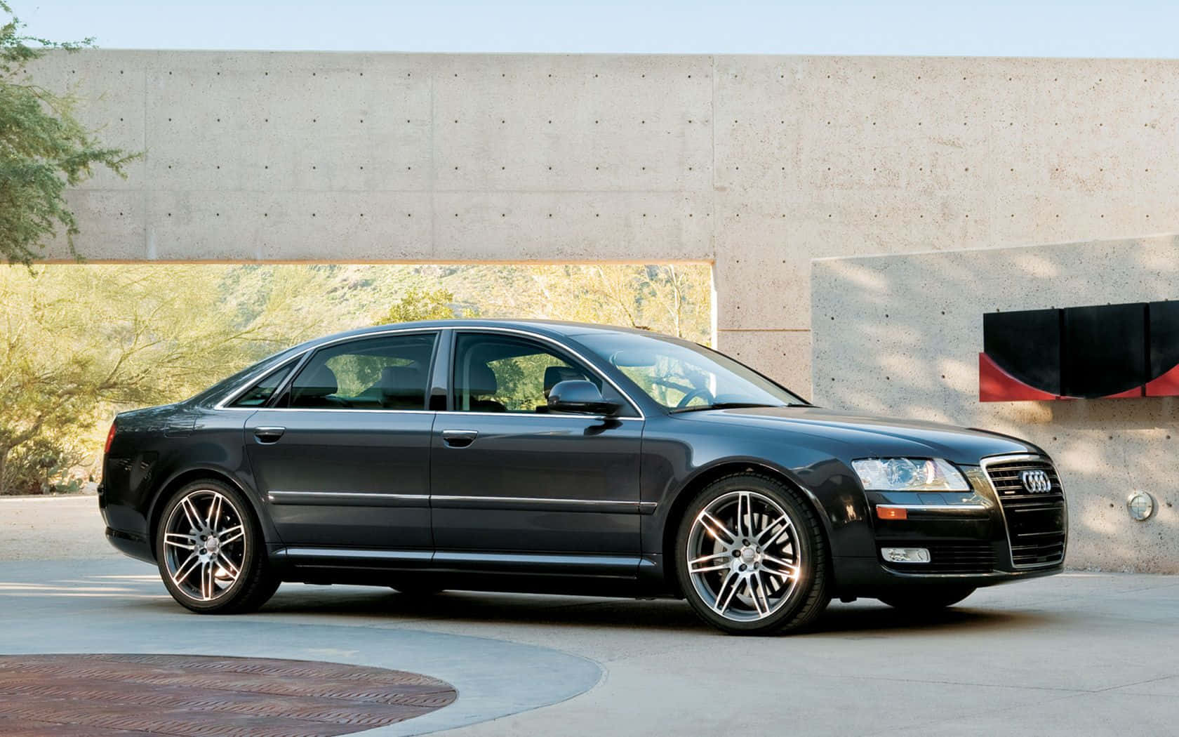 Audi S8 桌布 壁紙 — 一輛時尚的黑色奧迪轎車停在現代混凝土建築前，背景是沙漠植物。