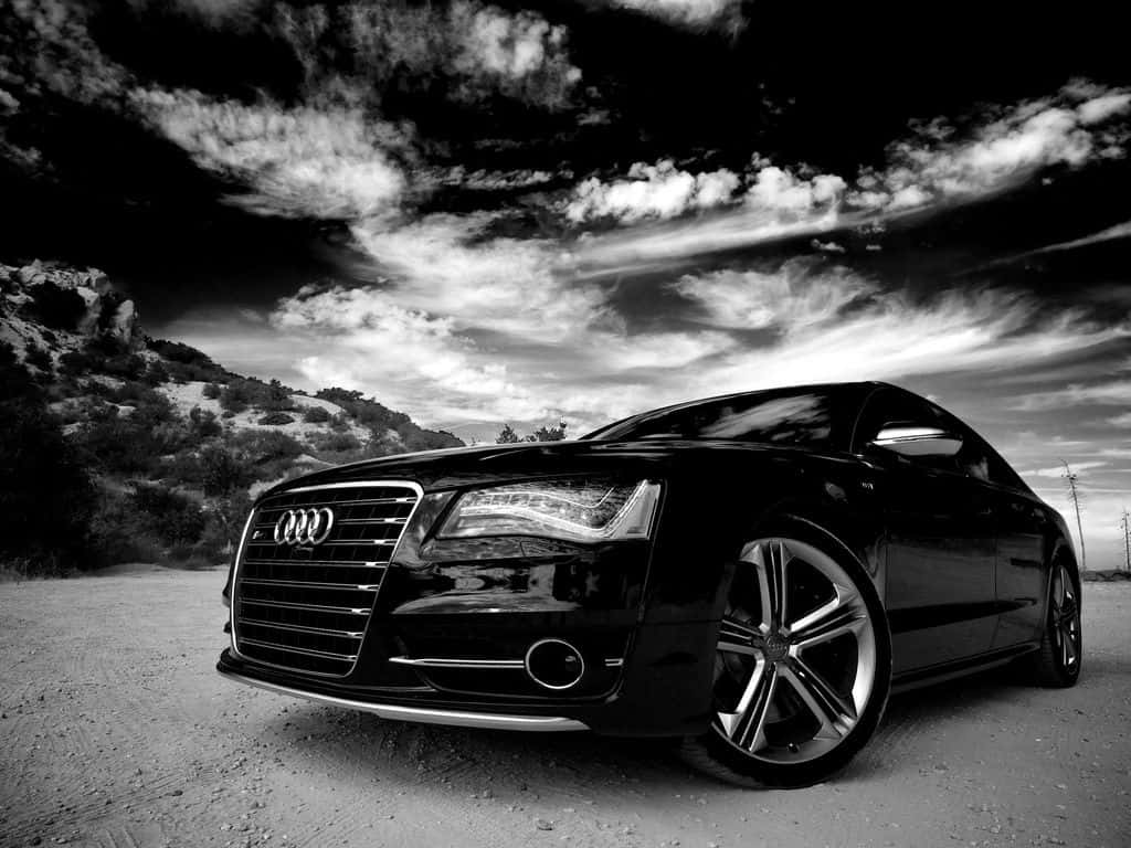 Audi S8 桌布 壁紙 — 一輛時尚的黑色奧迪轎車停泊在塵土飛揚的道路上，背景是戲劇性的多雲天空和岩石丘陵。