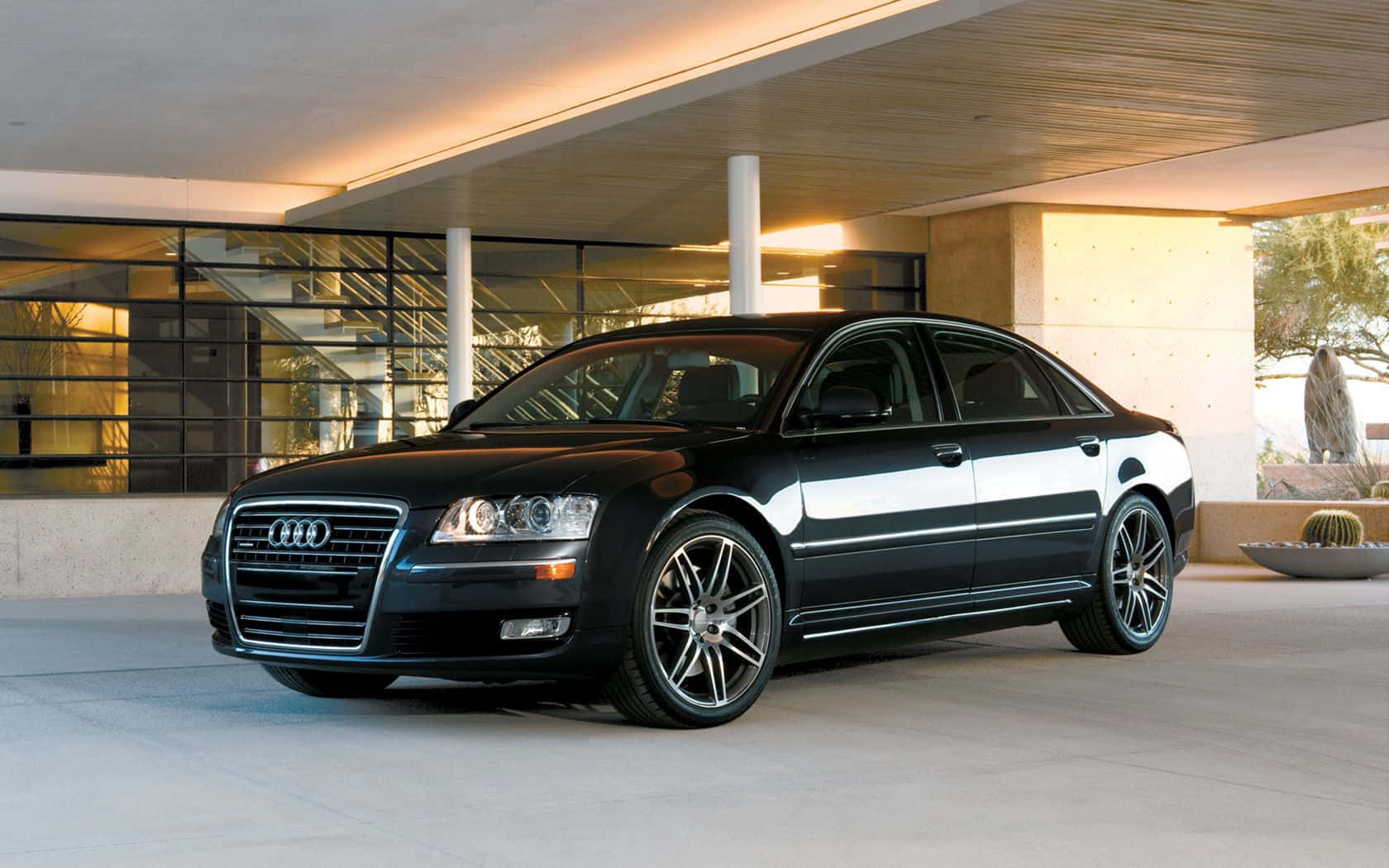 Audi S8 桌布 壁紙 — 一輛時尚的黑色奧迪轎車在現代玻璃和混凝土庭院中，在溫暖的建築燈光下閃閃發光。
