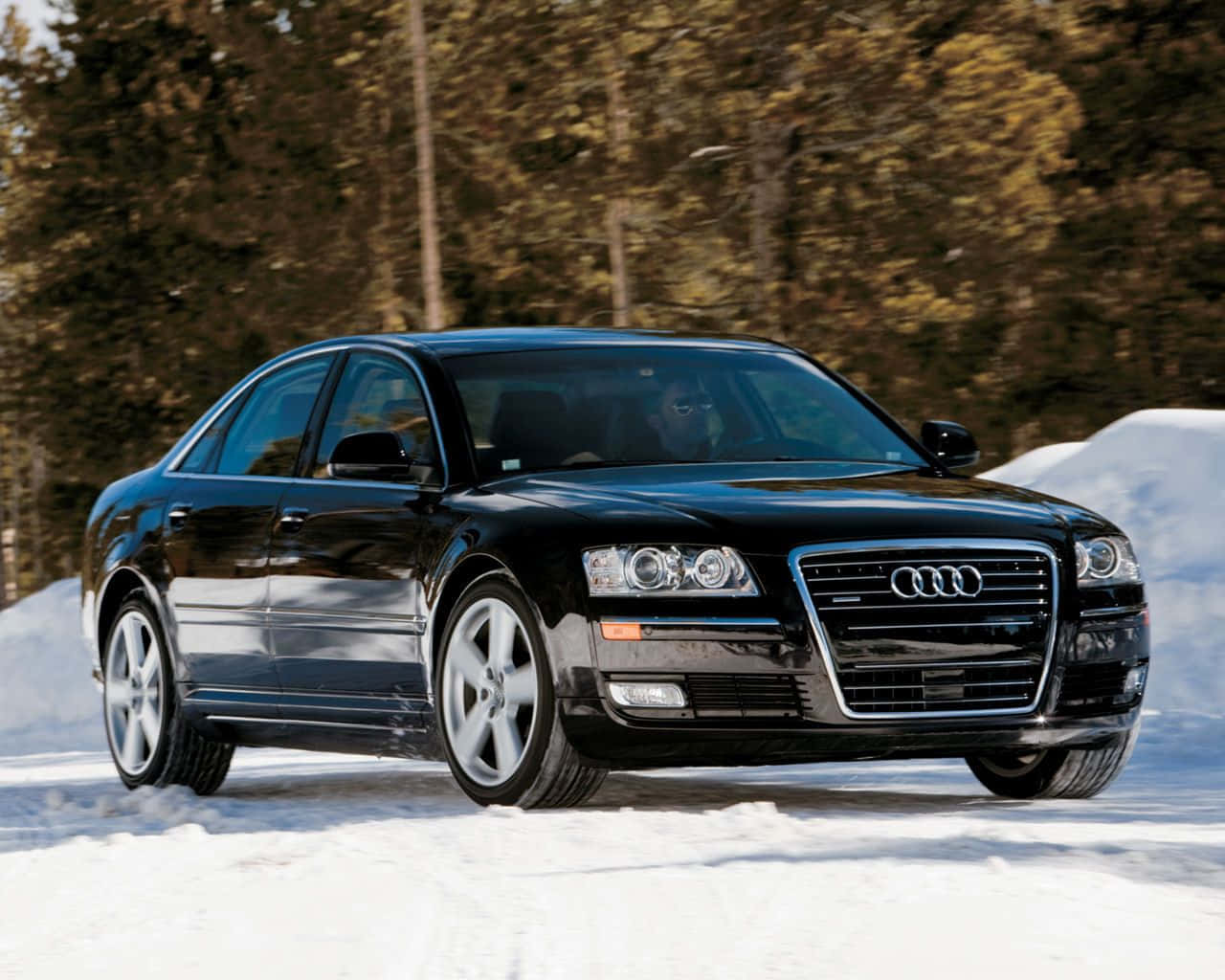 Audi S8 桌布 壁紙 — 一輛時尚的黑色奧迪轎車在雪地森林中行駛，背景是金棕色的樹木。