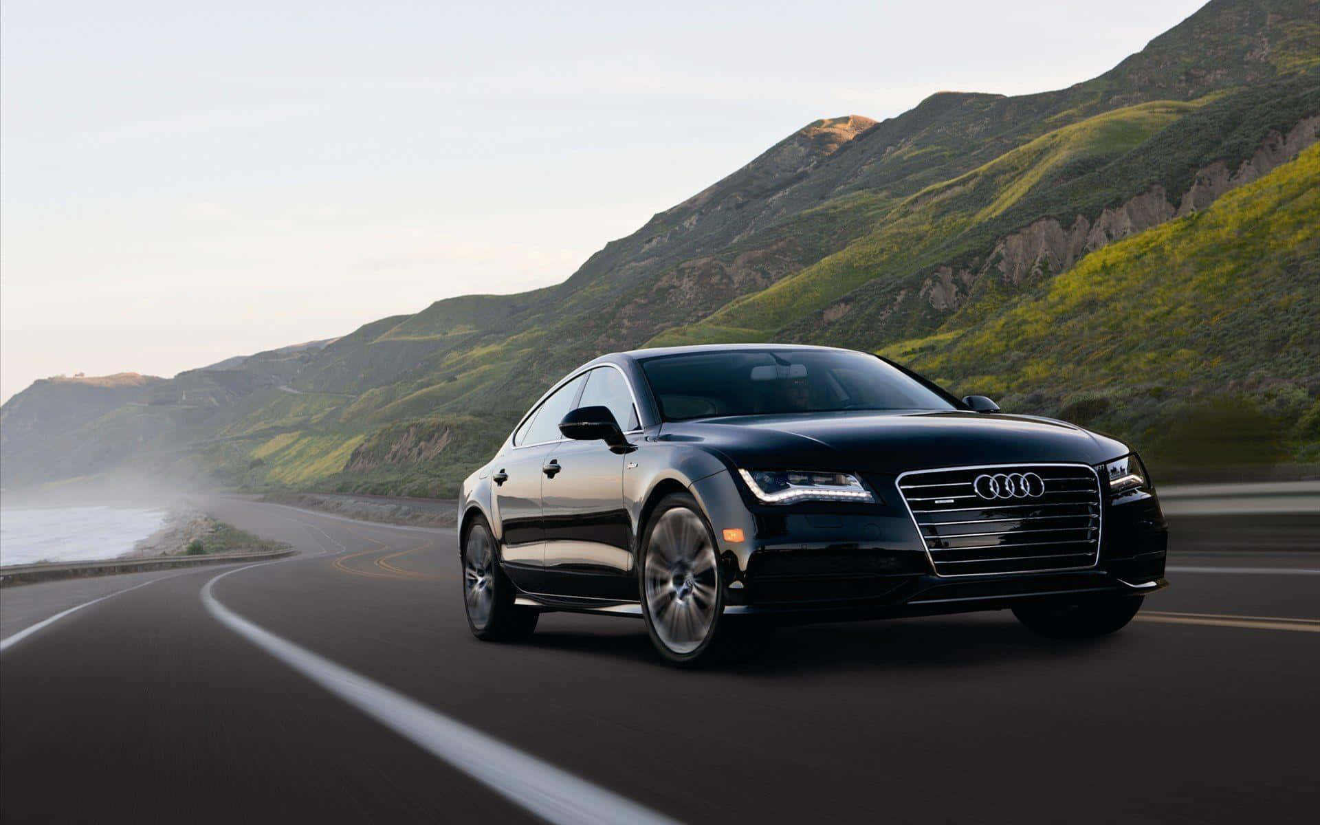 Audi S7 桌布 壁紙 — 一輛時尚的黑色奧迪轎車沿著海岸公路行駛，背景是翠綠的山丘和海洋薄霧。